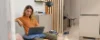 Eine Frau sitzt in einem modernen Wohnzimmer auf einem Sofa mit einem Laptop, umgeben von stilvollen Dekorationen von Nolte Living.