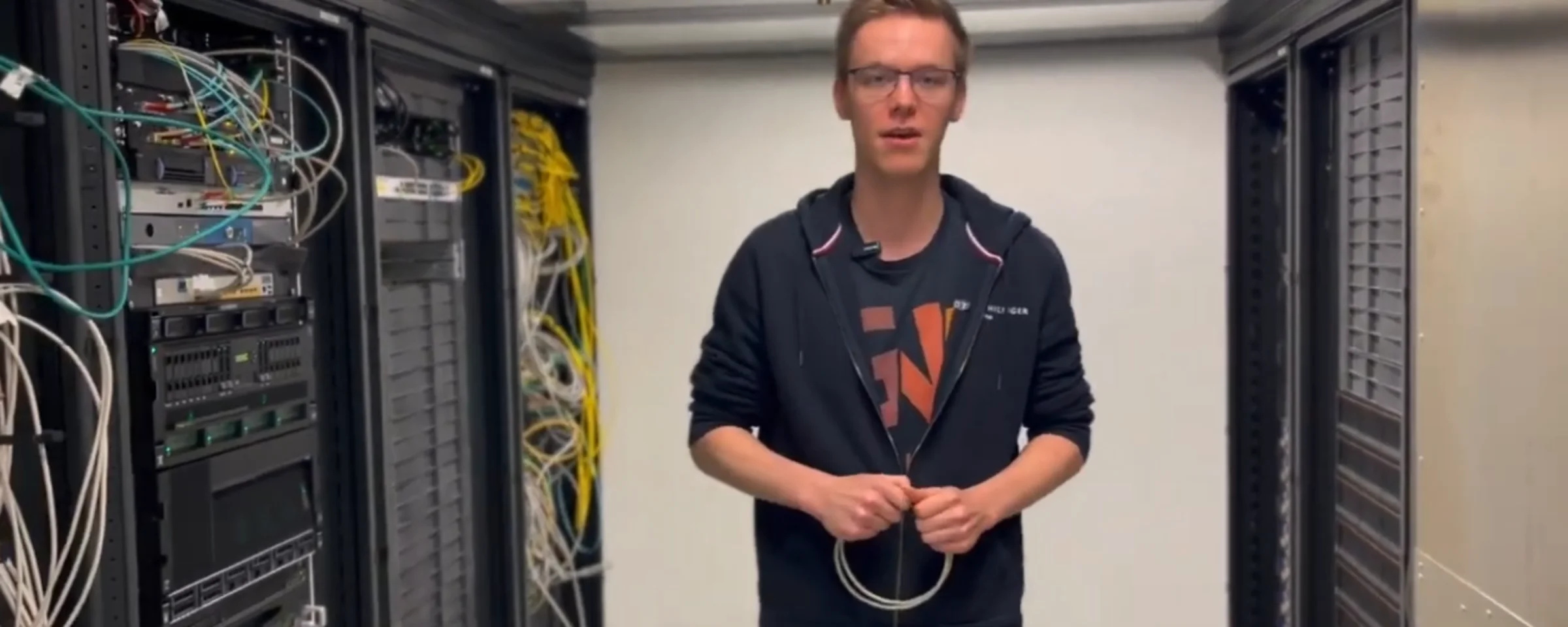 Ein Mann steht in einem Serverraum zwischen Regalen mit Kabeln und Technik.