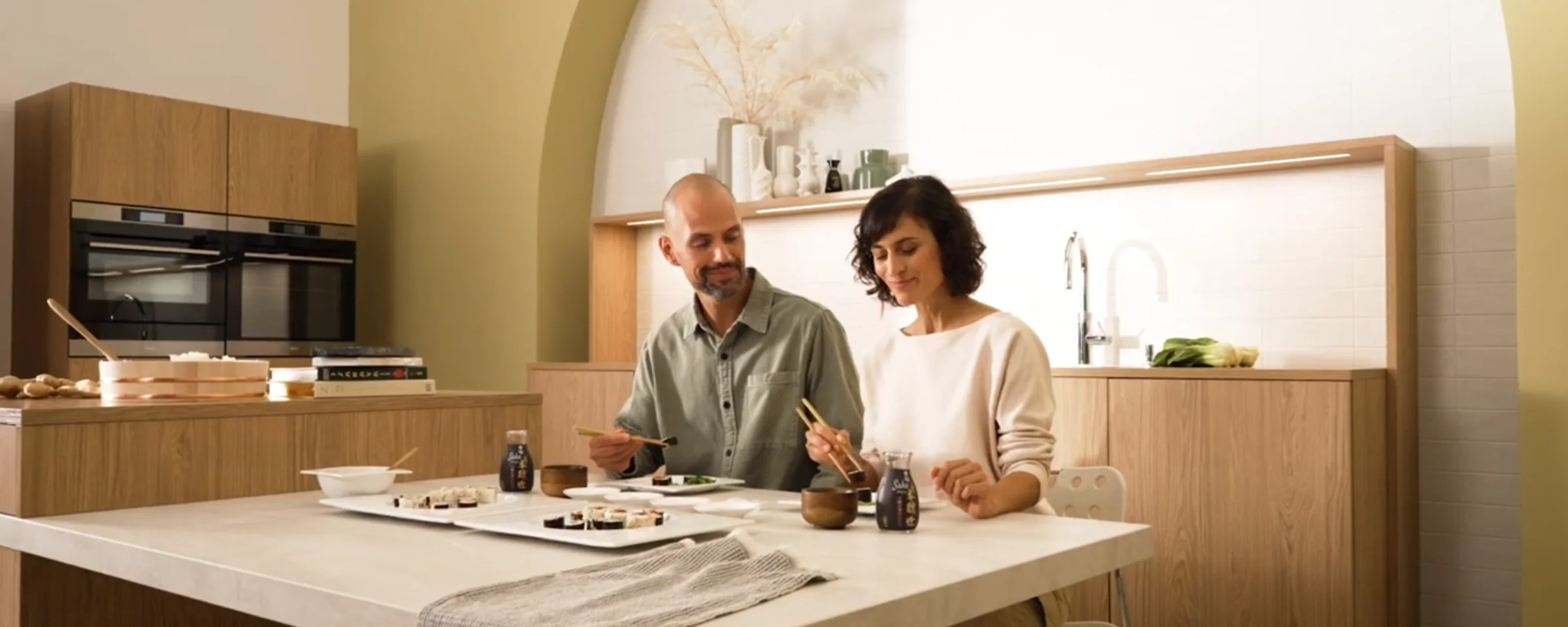 Ein Paar isst Sushi an einem Tisch in einer modernen Nolte Küchen Umgebung.