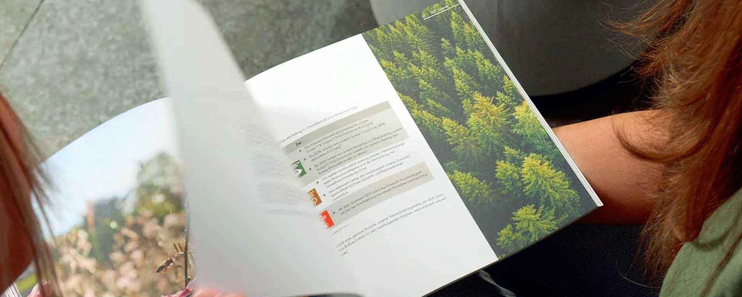 Zwei Personen blättern in einem Magazin mit Naturfotos, während sie auf einem grauen Sofa sitzen. Nolte Küchen.