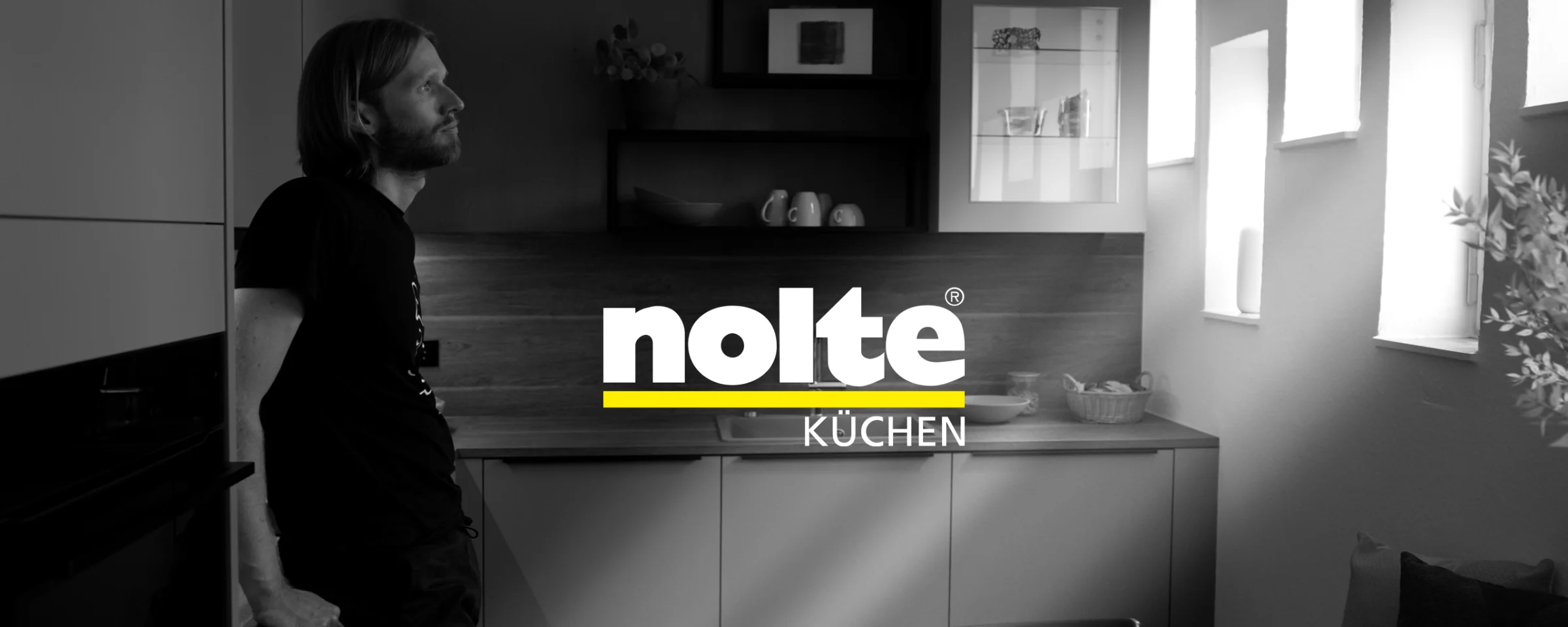 Mężczyzna opiera się o blat w nowoczesnej kuchni Nolte Kitchen.