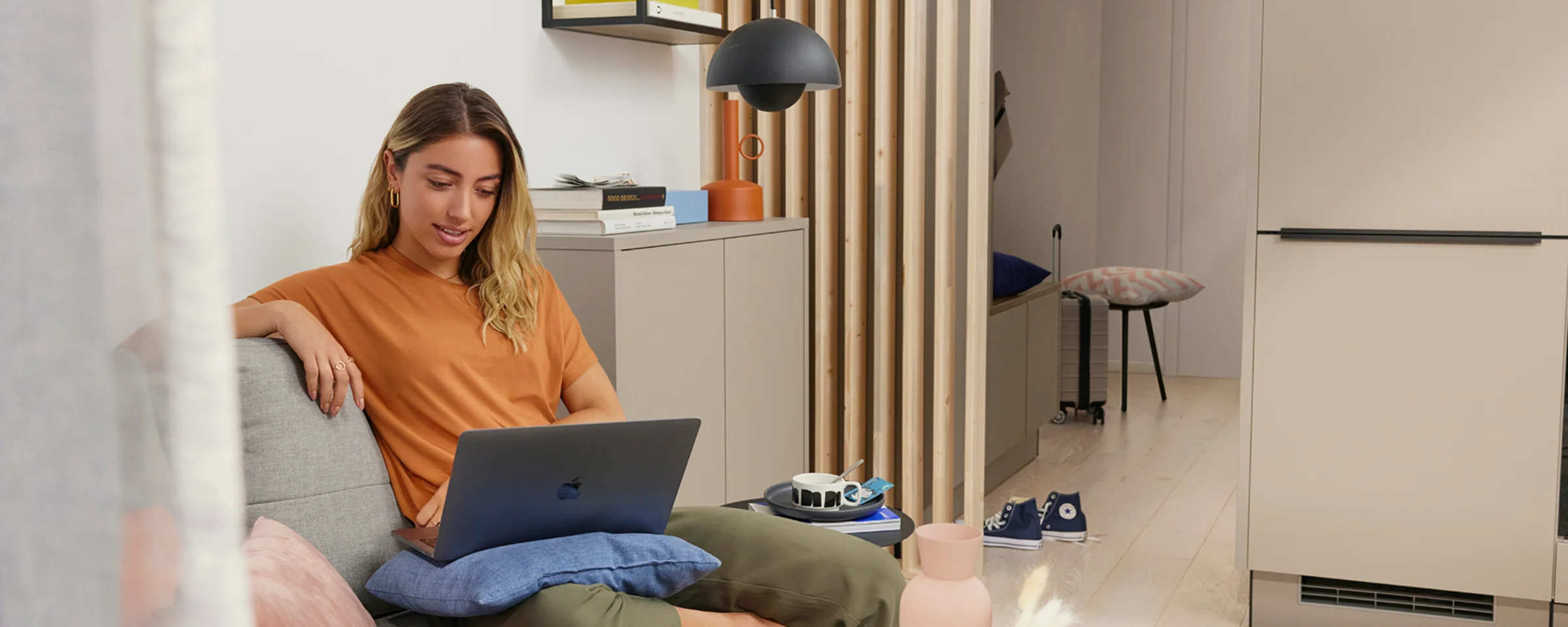 Eine Frau sitzt in einem modernen Wohnzimmer auf einem Sofa mit einem Laptop, umgeben von stilvollen Dekorationen von Nolte Living.