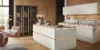 Una cocina moderna con armarios blancos y detalles de madera de Nolte Cocina.