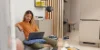 Eine Frau sitzt in einem modernen Wohnzimmer auf einem Sofa mit einem Laptop, umgeben von stilvollen Dekorationen von Nolte Living.