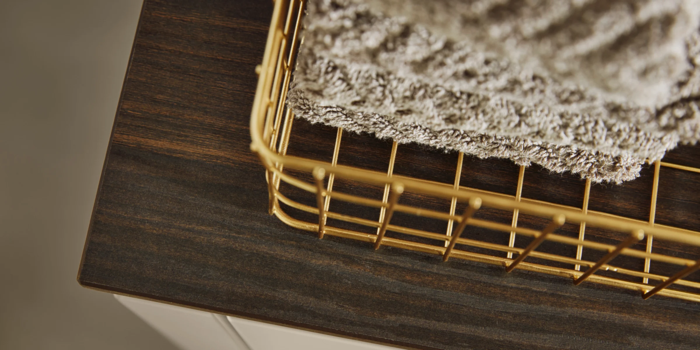 Ein goldener Korb mit Handtüchern steht auf einem dunklen Holzregal von Nolte Living.
