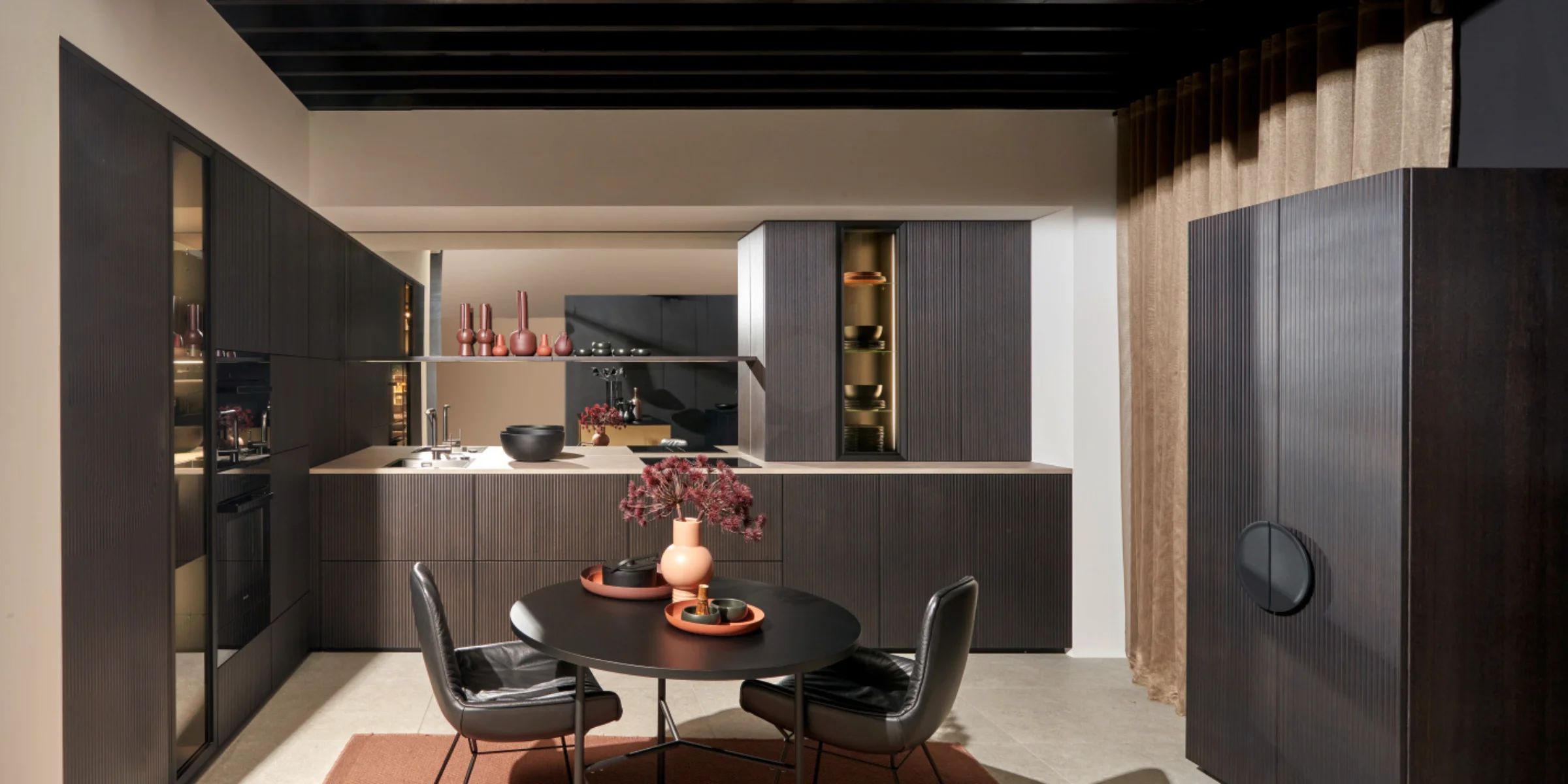 A modern kitchen with dark cabinets and a round dining table, Nolte Küchen.