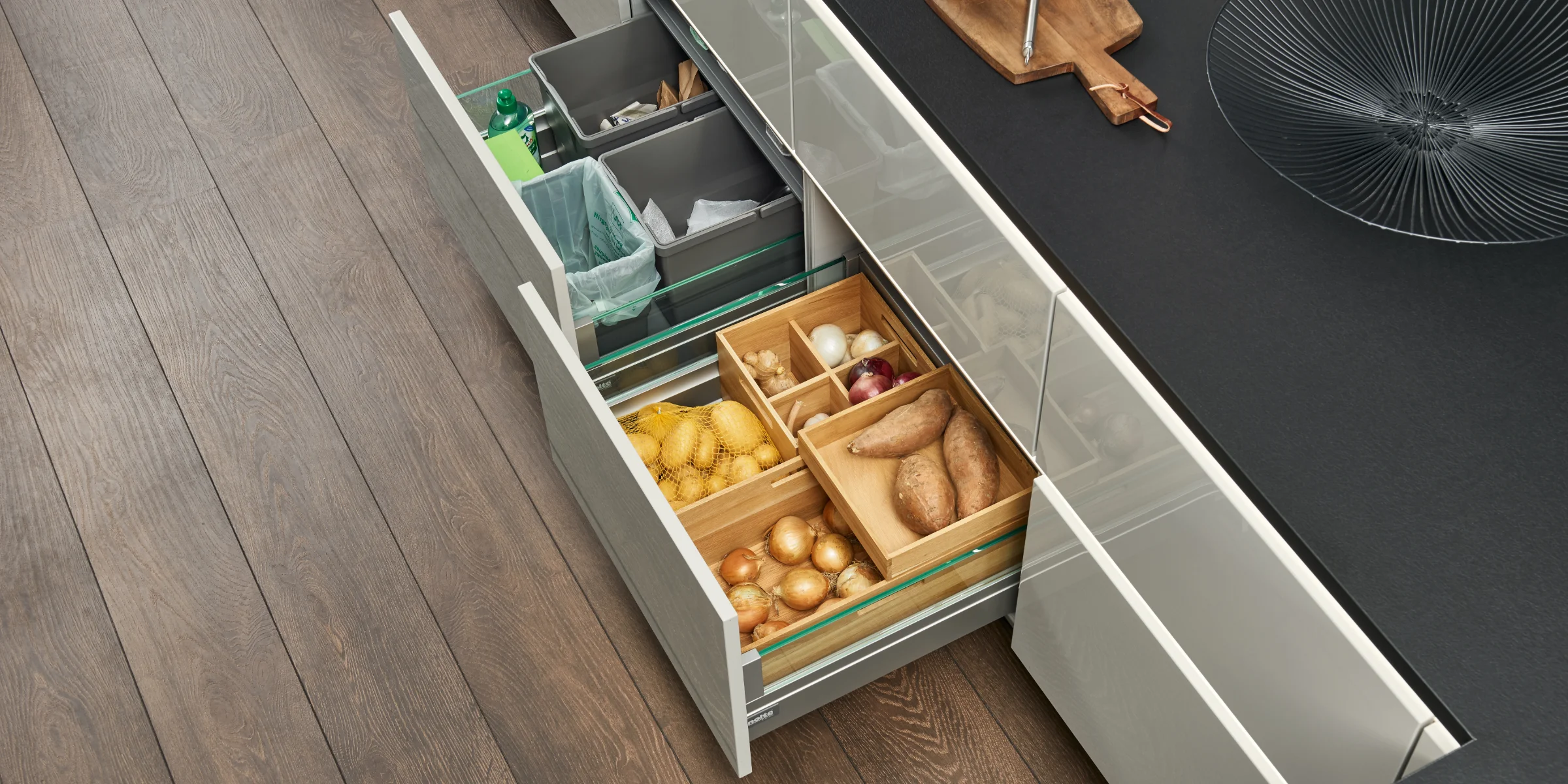 In einer modernen Küche mit Holzfußboden sind offene Schubladen mit Vorräten zu sehen. Nolte Küchen.