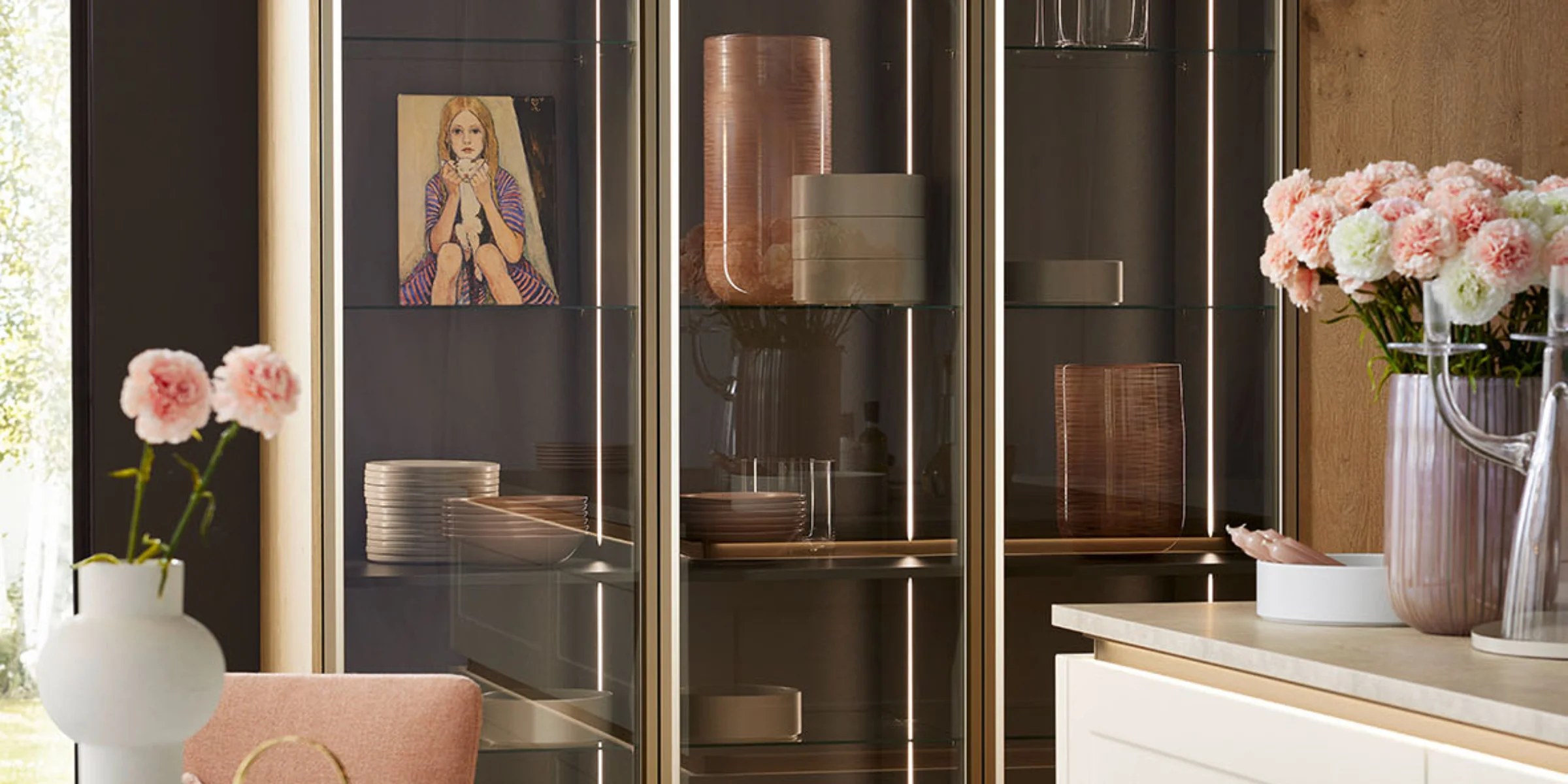 Una cocina moderna con vitrinas de vidrio y frentes de madera, decorada con flores y arte, de Nolte Cocina.