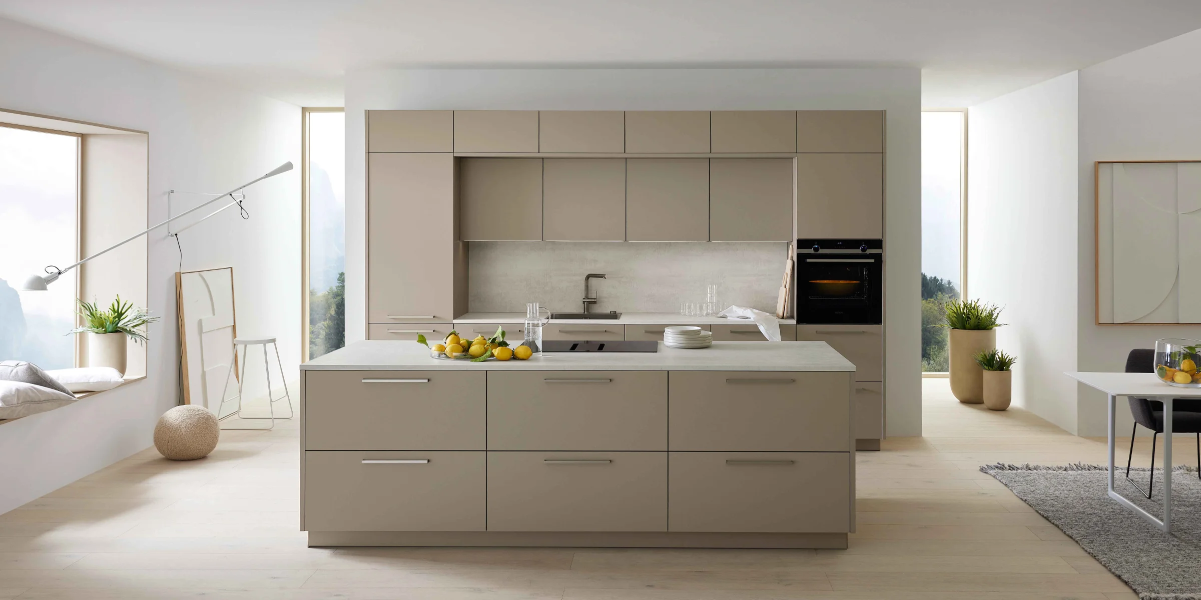 Eine moderne Küche mit Insel, hellen Schränken und großen Fenstern, gestaltet von Nolte Küchen.