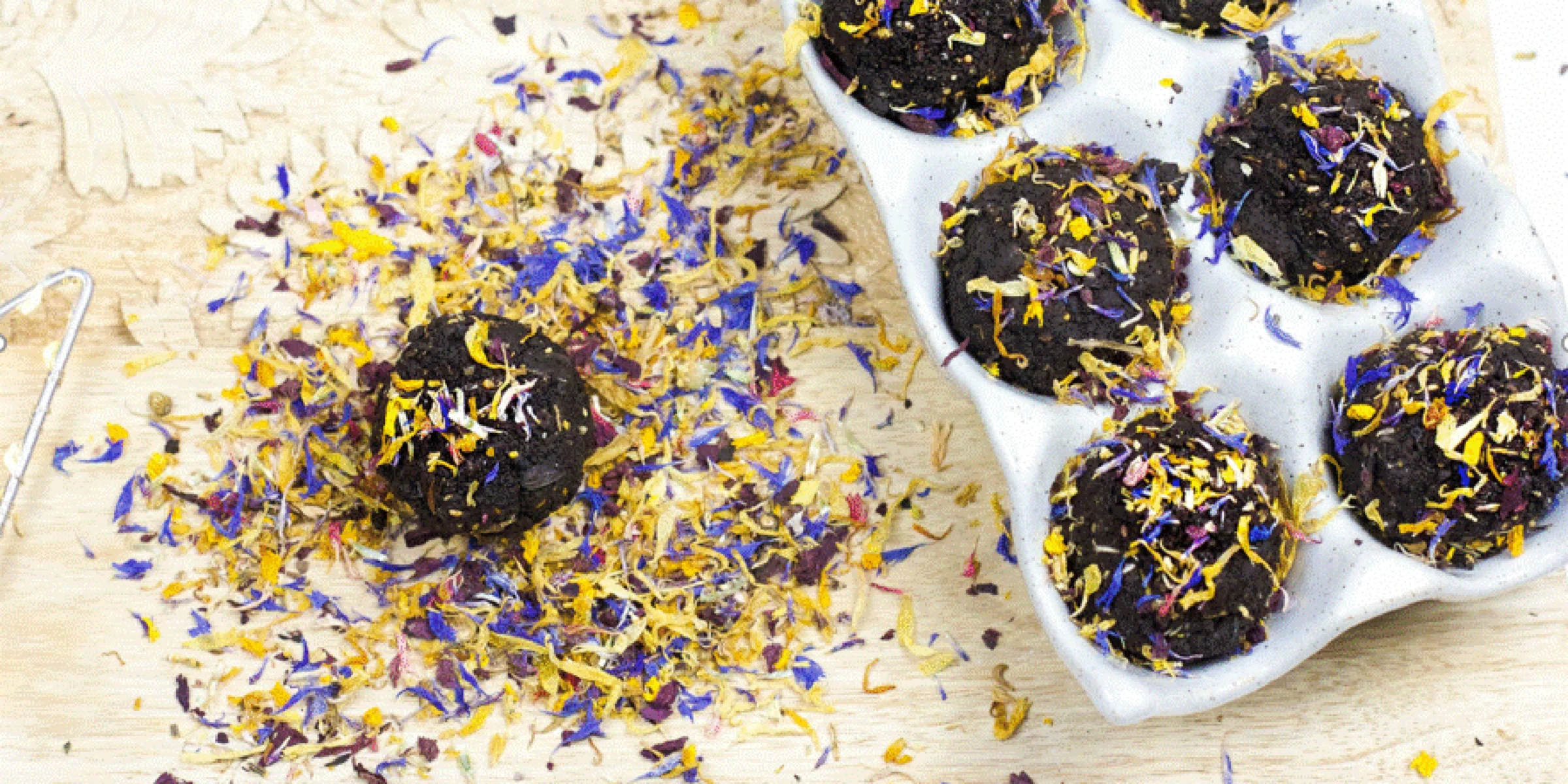 Eine Eierschachtel mit Schokoladenmuffins, dekoriert mit getrockneten Blüten, liegt auf einem hölzernen Brett.