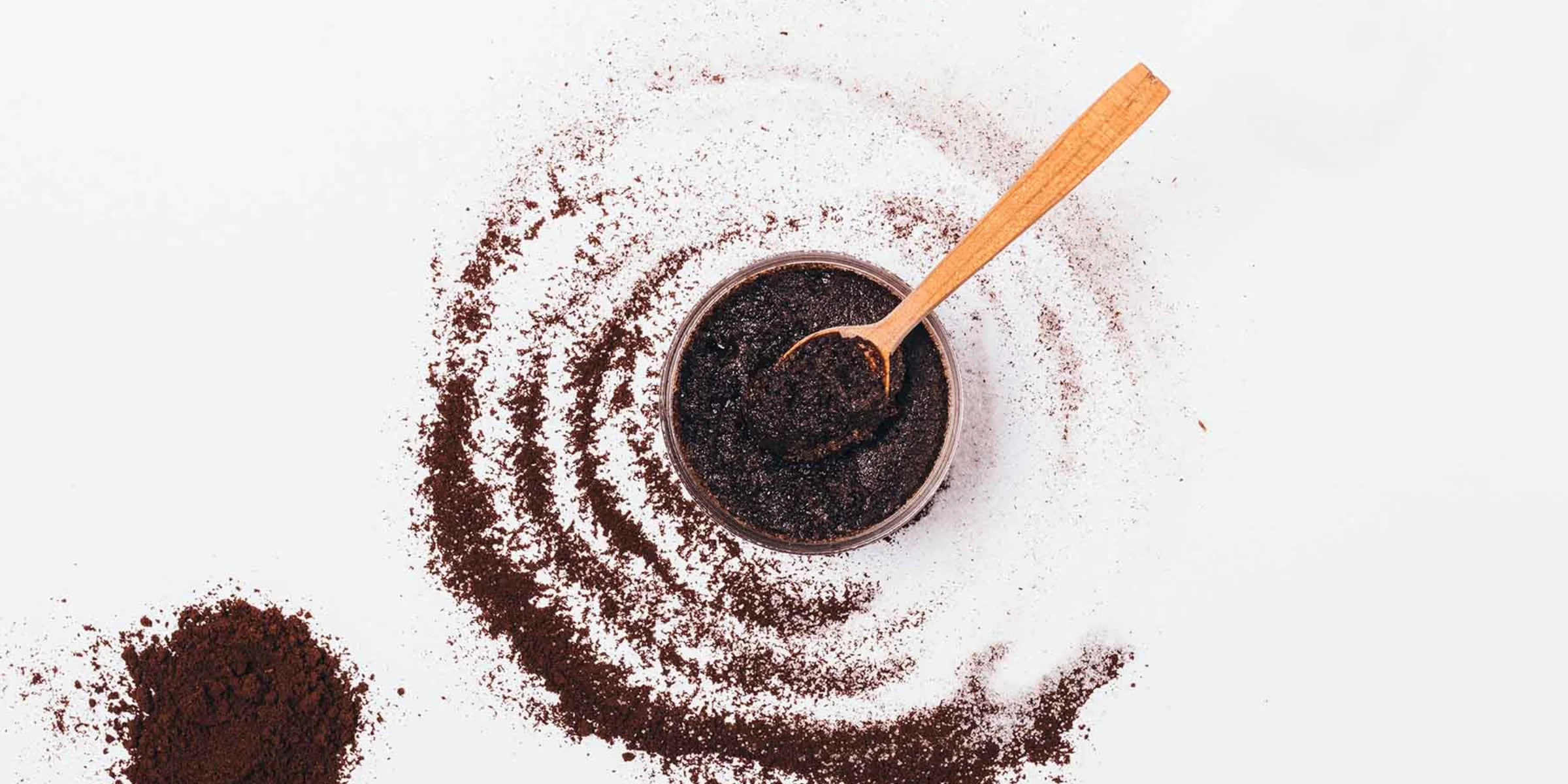 Un cuenco con café molido y una cuchara de madera, rodeado de café molido esparcido.