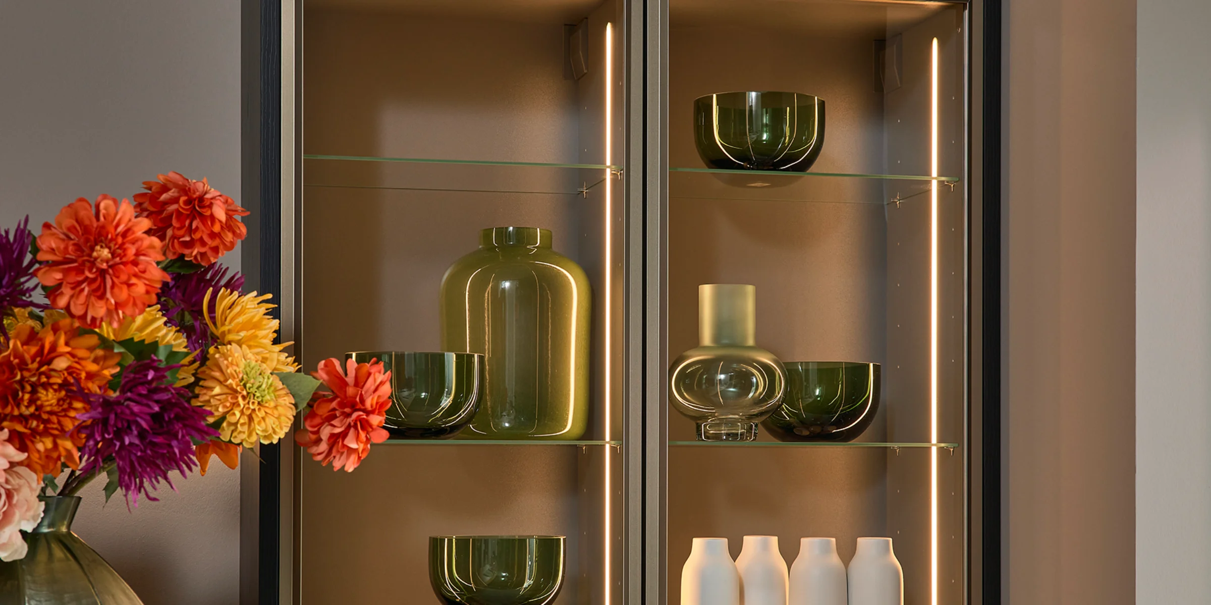 A stylish kitchen cabinet with glass shelves and decorative lighting, arranged by Nolte Kitchens.