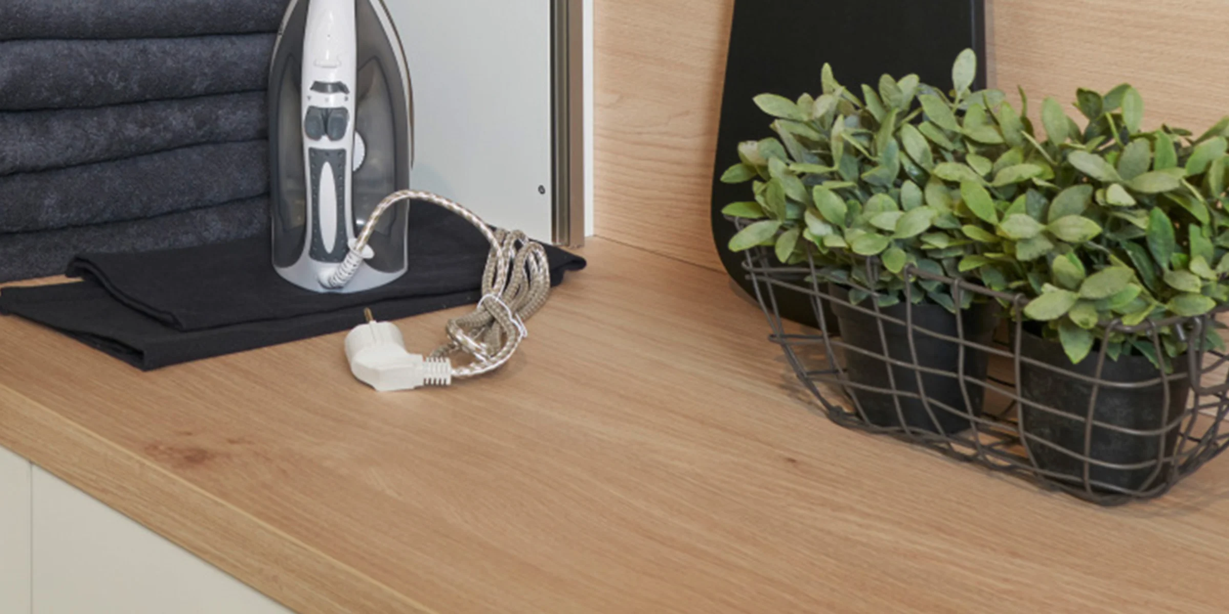 Ein Bügeleisen und Pflanzen stehen auf einer Arbeitsplatte in einem Hauswirtschaftsraum von Nolte Hauswirtschaftsräume.