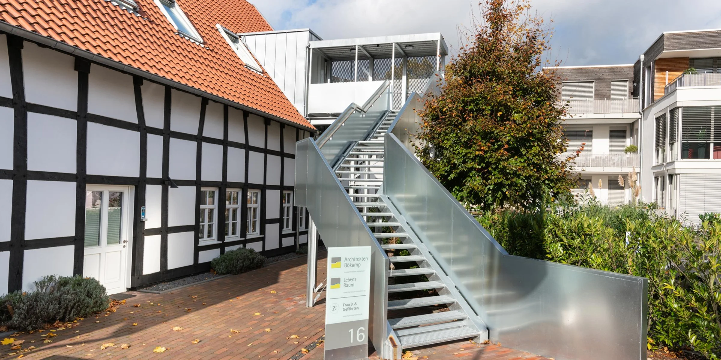 Ein modernes Gebäude mit Außentreppe neben einem Fachwerkhaus bei bewölktem Himmel.