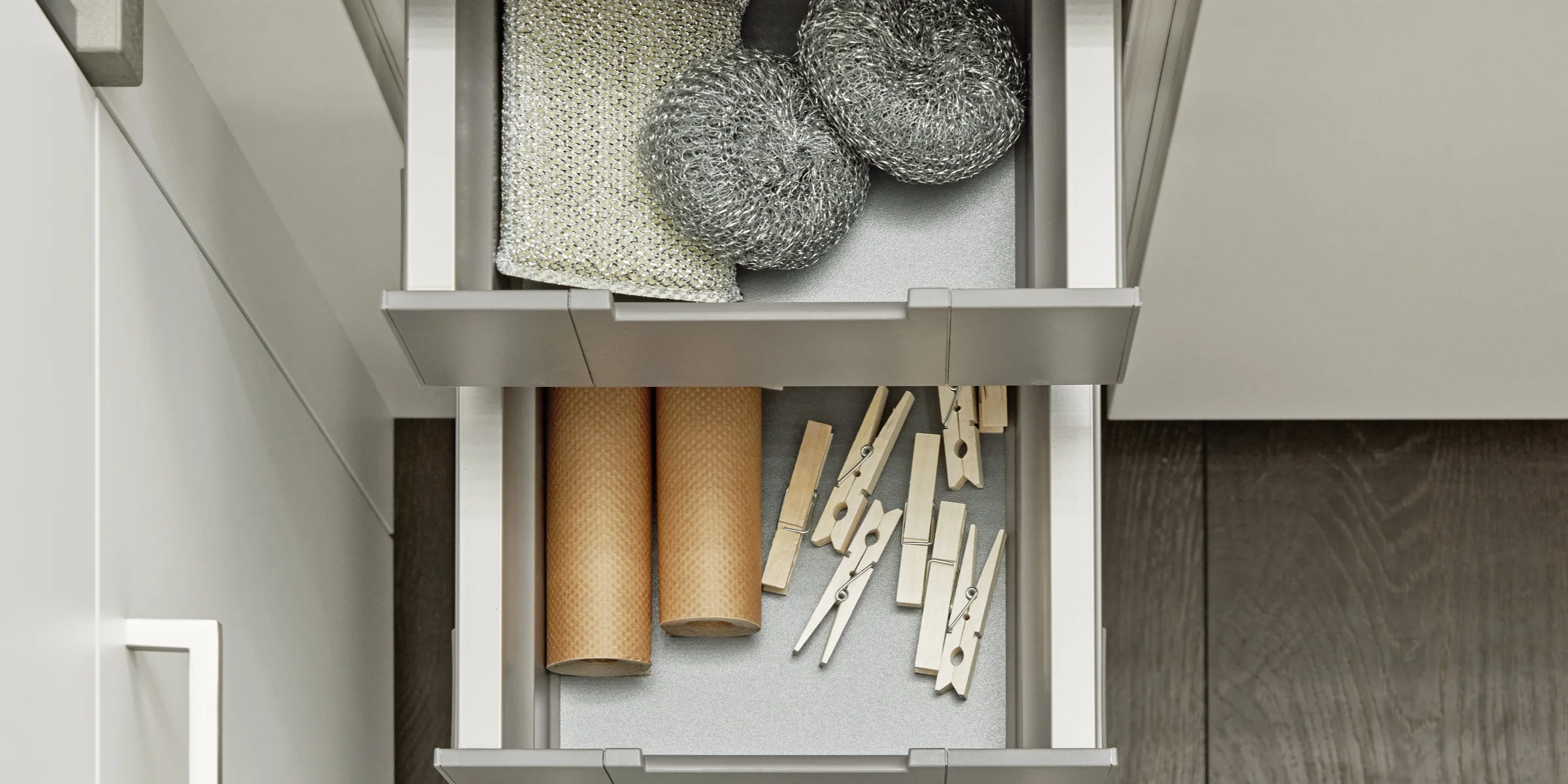 Ein geöffneter Küchenschrank mit Schubladen voller Reinigungsutensilien, entworfen von Nolte Hauswirtschaftsräume.