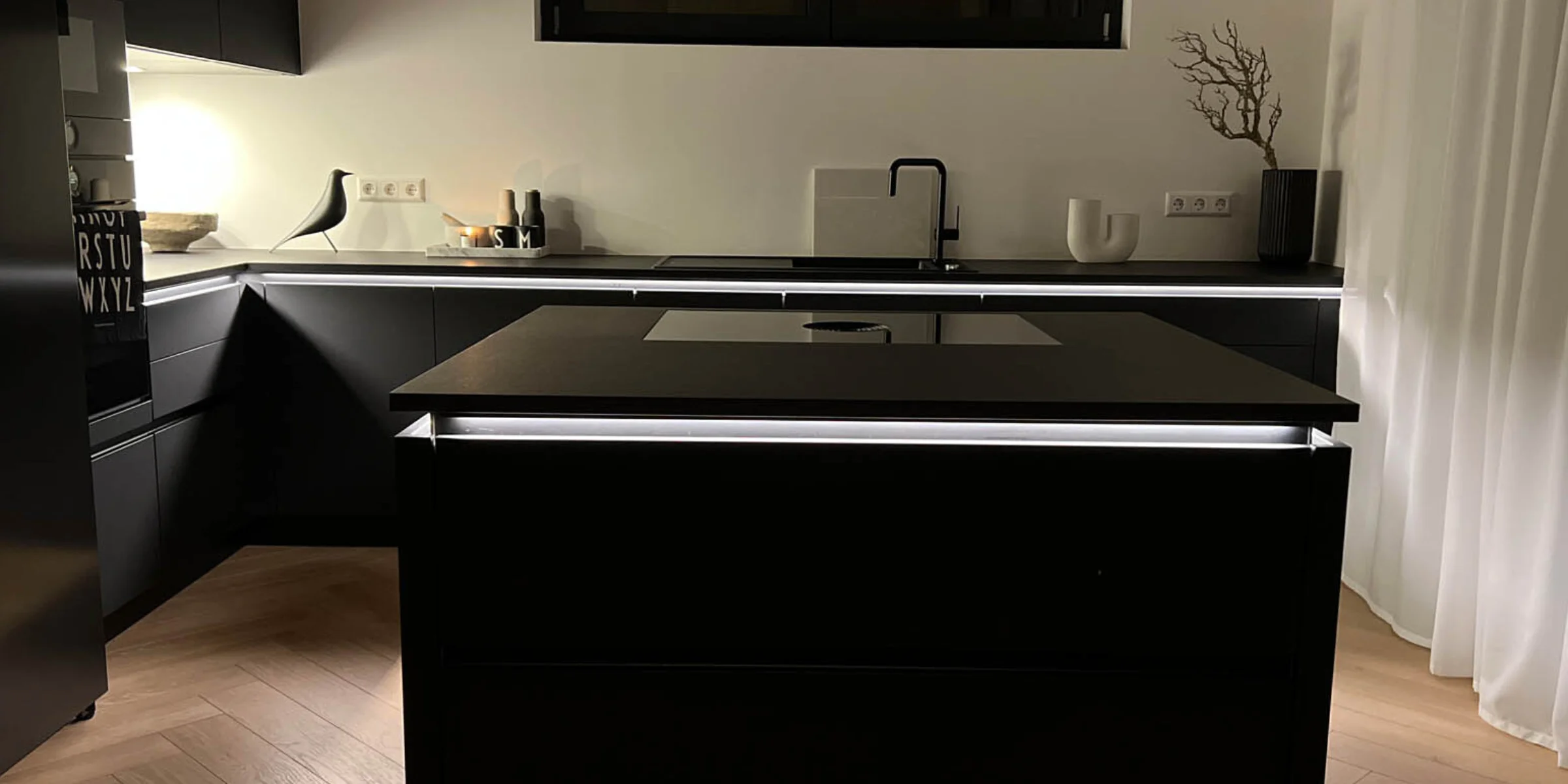 Eine moderne, dunkle Küche mit Insel und Beleuchtung, gestaltet von Nolte Küchen.