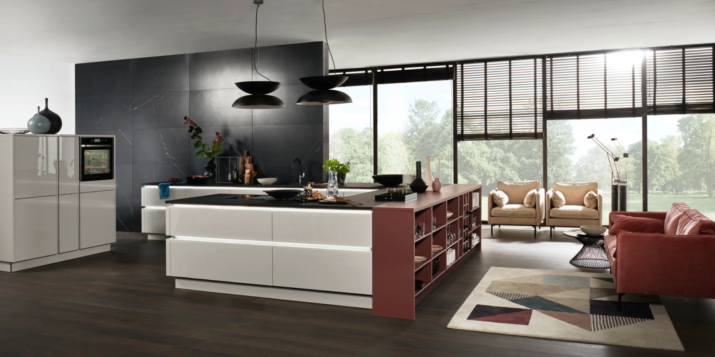  Moderne Nolte Küche mit der hochglänzenden Front NOVA LACK Platingrau. Die grifflose Inselküche besticht durch klare Linien, eine großzügige Arbeitsfläche mit integriertem Kochfeld und eine offene Regalfläche in warmem Rotbraun. Der Raum wirkt offen und lichtdurchflutet dank bodentiefer Fenster und eleganter Einrichtung mit gemütlicher Sitzecke im Wohnzimmerstil.