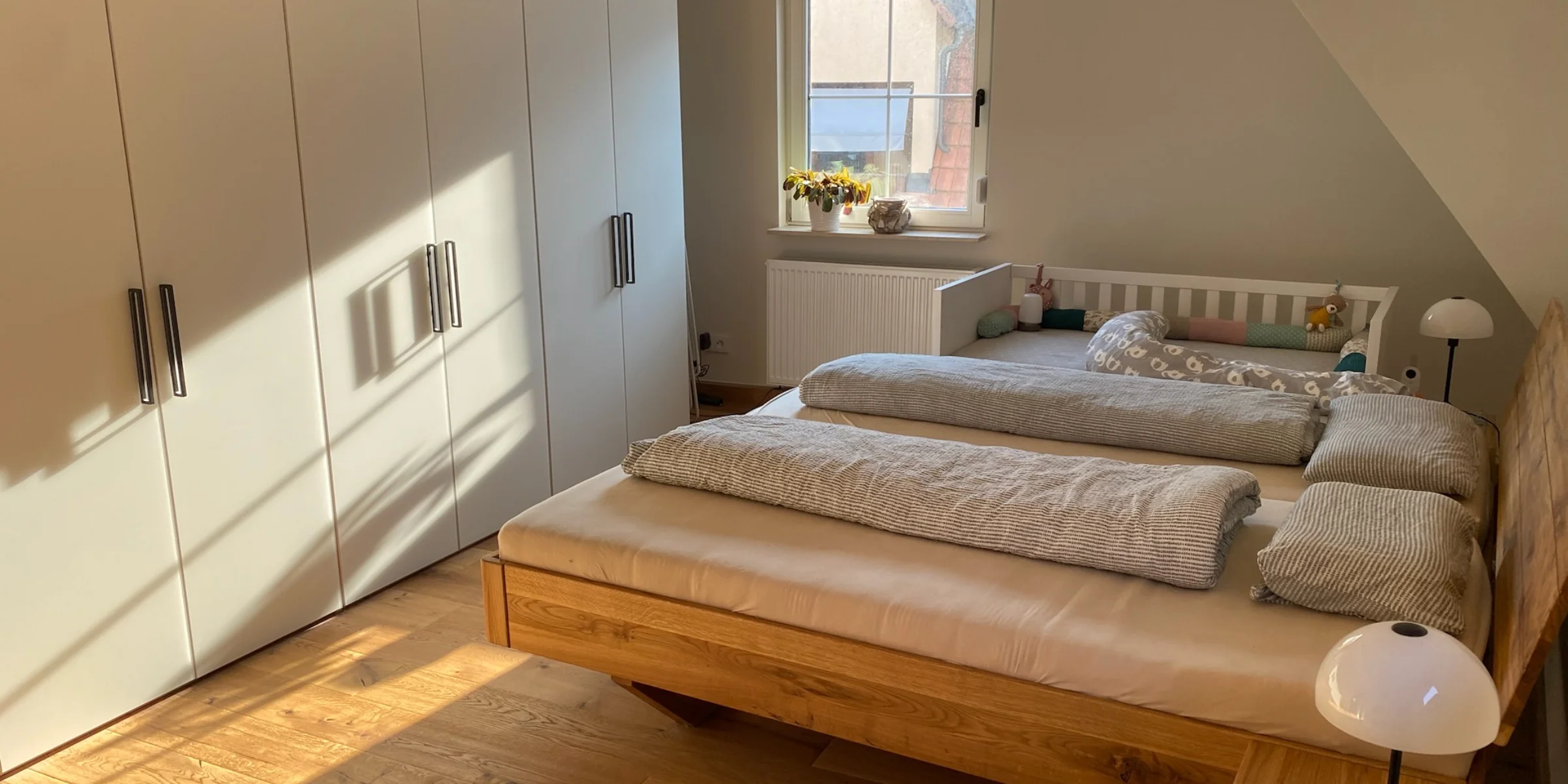 Ein Schlafzimmer mit einem Doppelbett und Kleiderschrank, beleuchtet von Sonnenlicht, gehört zu Nolte Living.