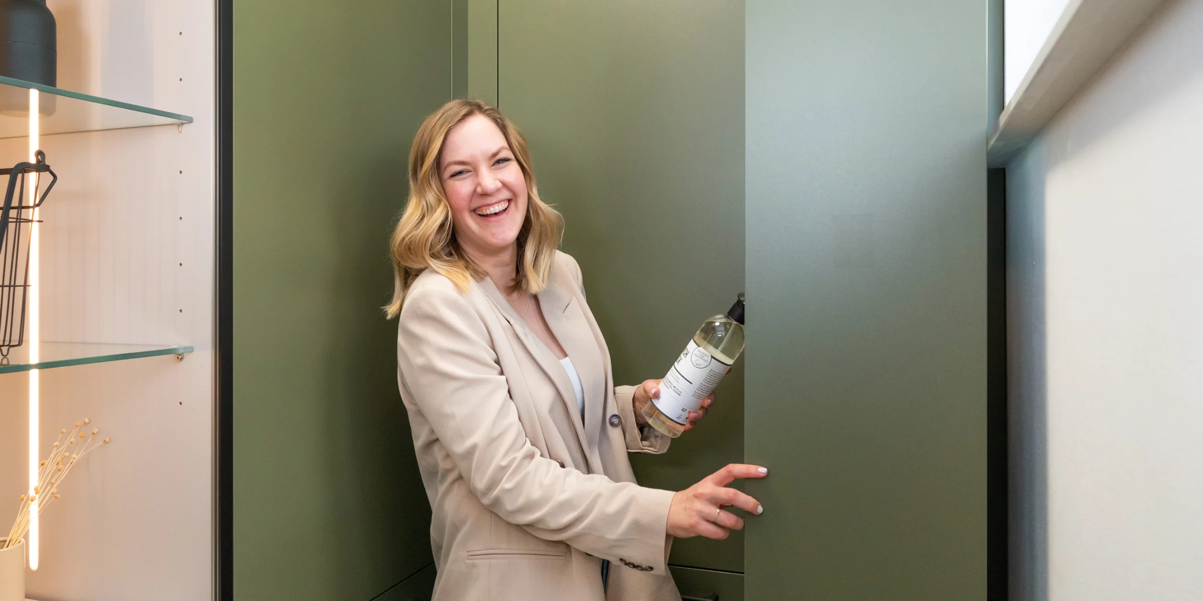 Eine Frau steht lächelnd in einem modernen Nolte Hauswirtschaftsraum mit grünen Schränken.
