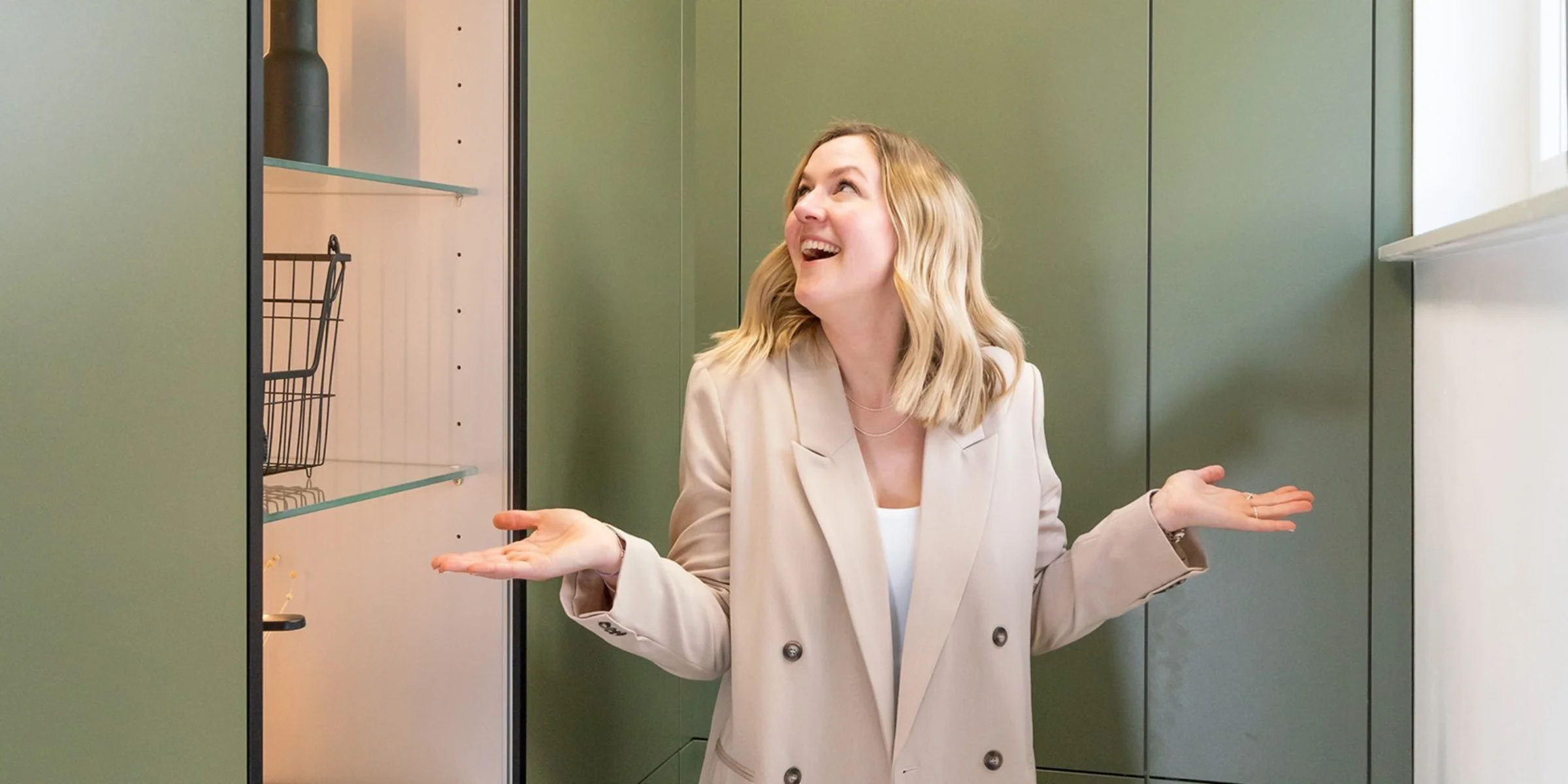 Eine Frau steht in einem modernen Hauswirtschaftsraum mit grünen Schränken von Nolte Hauswirtschaftsräume.