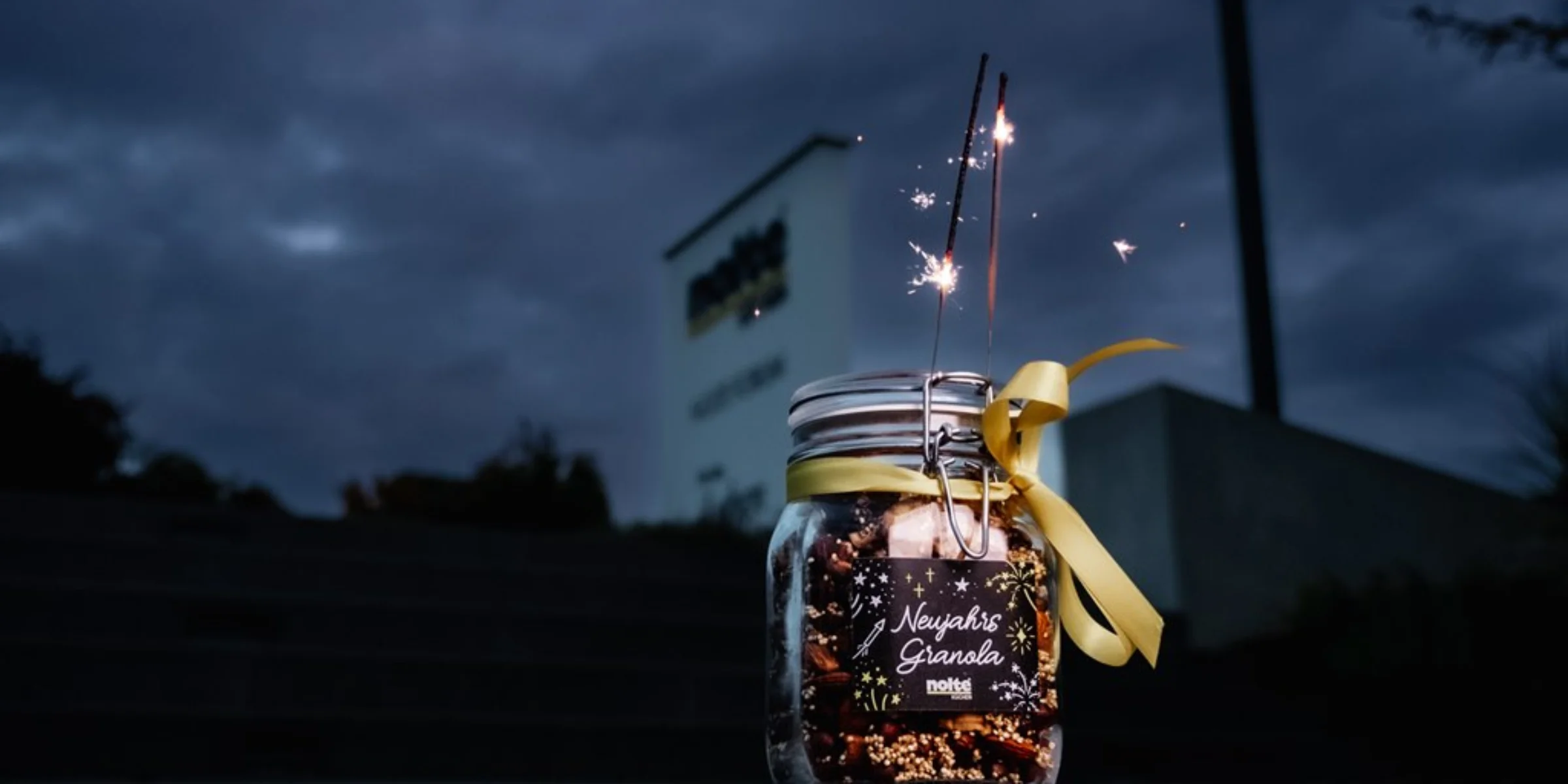 Ein Glas mit Wunderkerzen und gelber Schleife vor einem Schild bei Nacht.