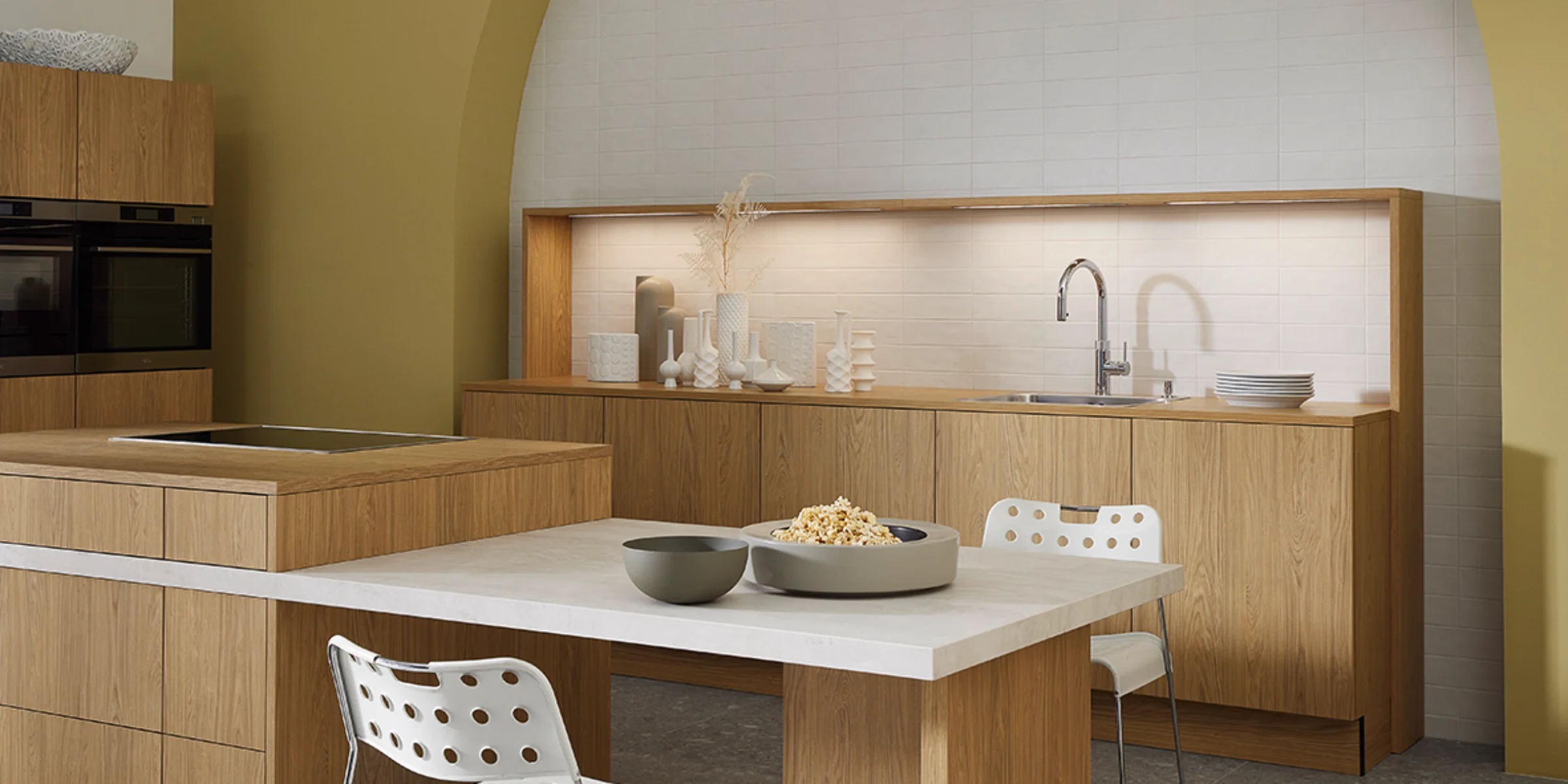 Moderne Küche mit Holzfronten und integriertem Essbereich vor gelber Akzentwand. Nolte Küchen.