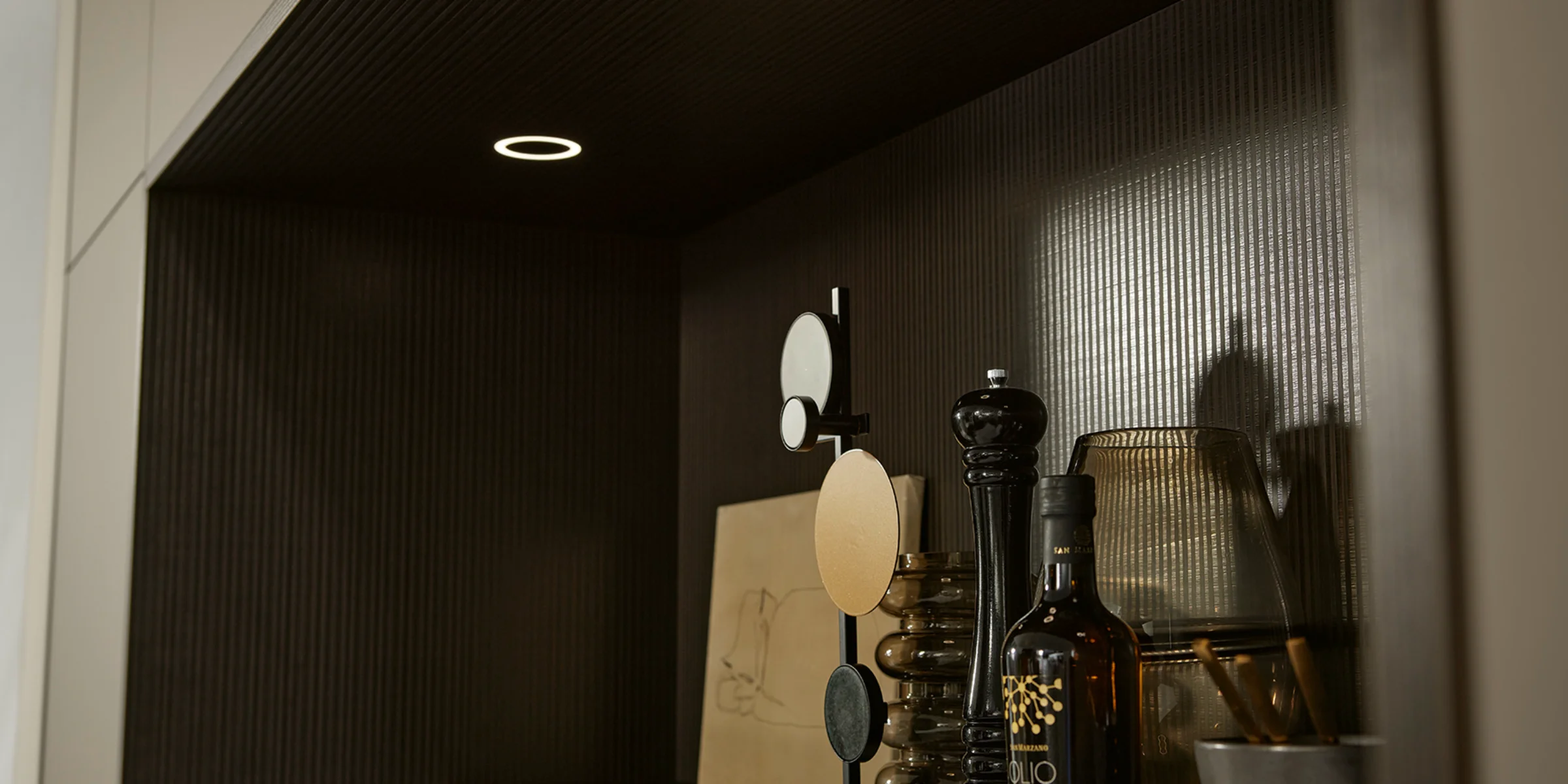 Ein Regal mit Gewürzen und Deko-Objekten, beleuchtet durch Einbauspots. Nolte Küchen.