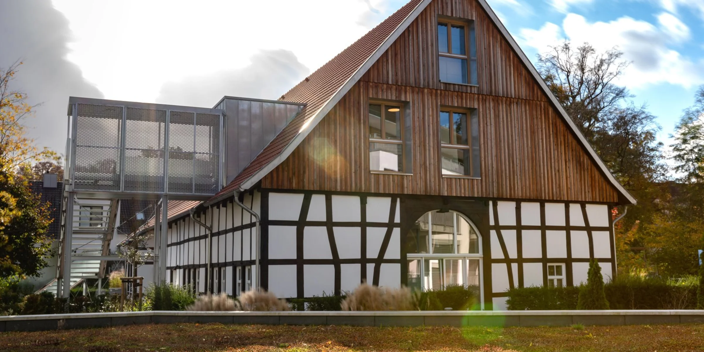 Ein modernes Fachwerkhaus umgeben von Bäumen steht im Sonnenlicht.