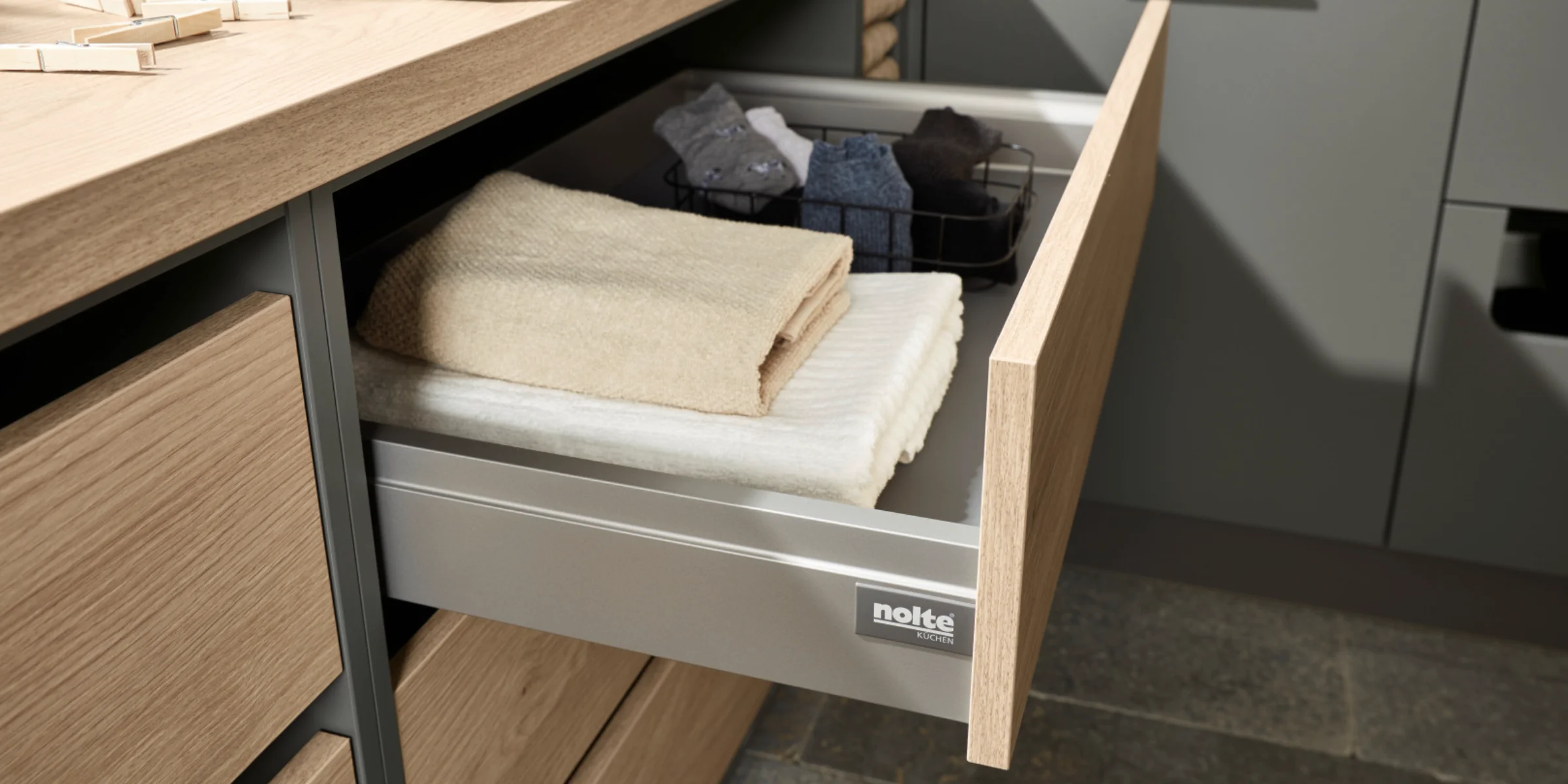 Ein geöffneter Schubladenschrank mit Handtüchern und Kleidungsstücken in einem Hauswirtschaftsraum von Nolte Hauswirtschaftsräume.