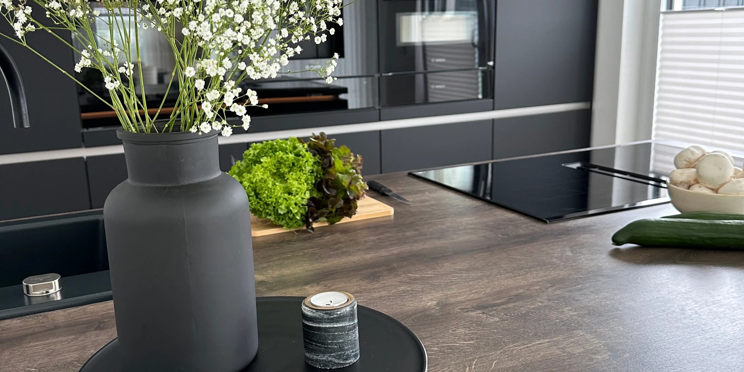 In einer modernen Küche mit dunklen Schränken steht eine Vase mit Blumen auf der Arbeitsplatte. Nolte Küchen.