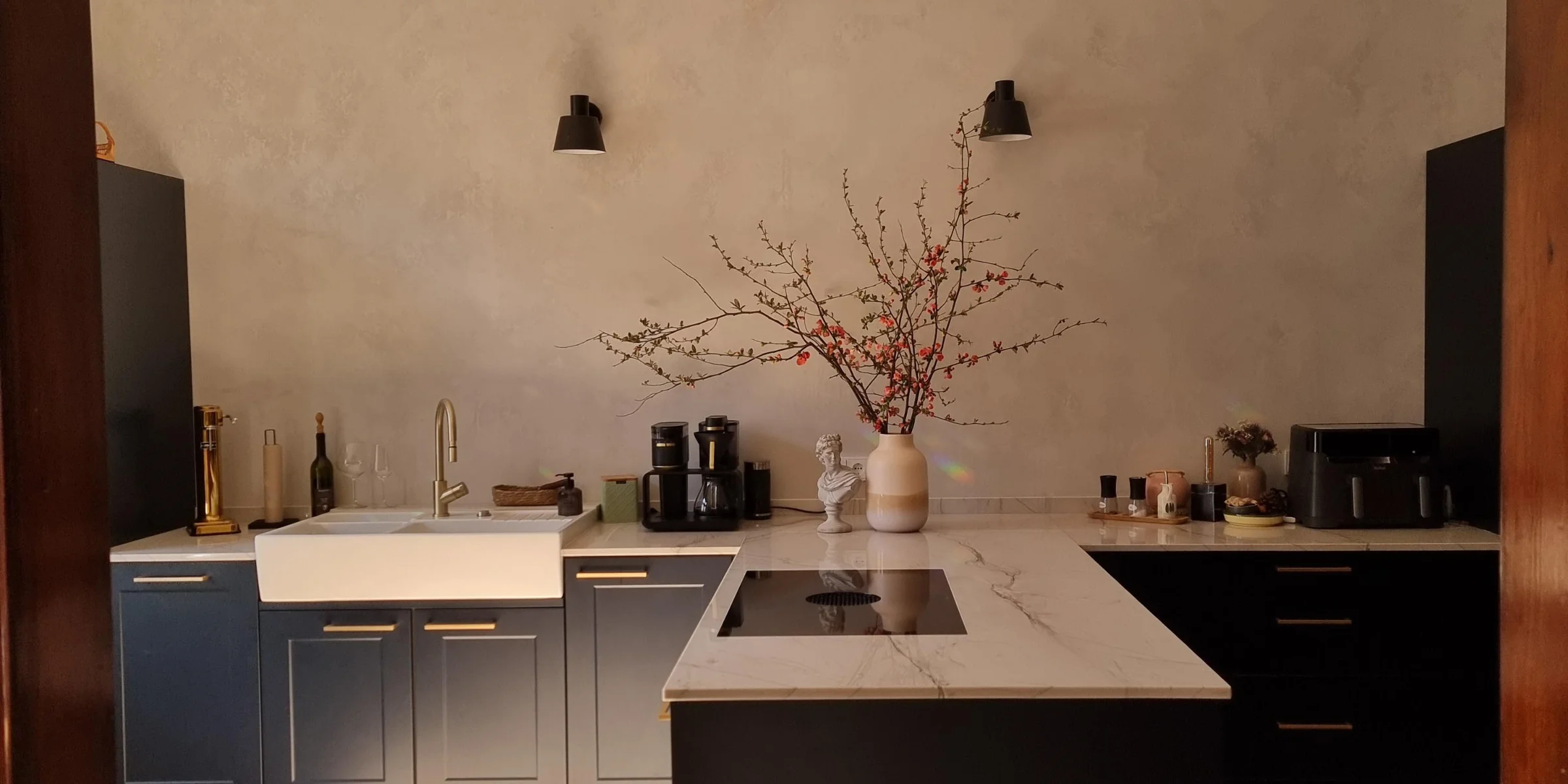 Cocina moderna con isla y armarios oscuros, iluminada por un candelabro. Nolte Cocina.