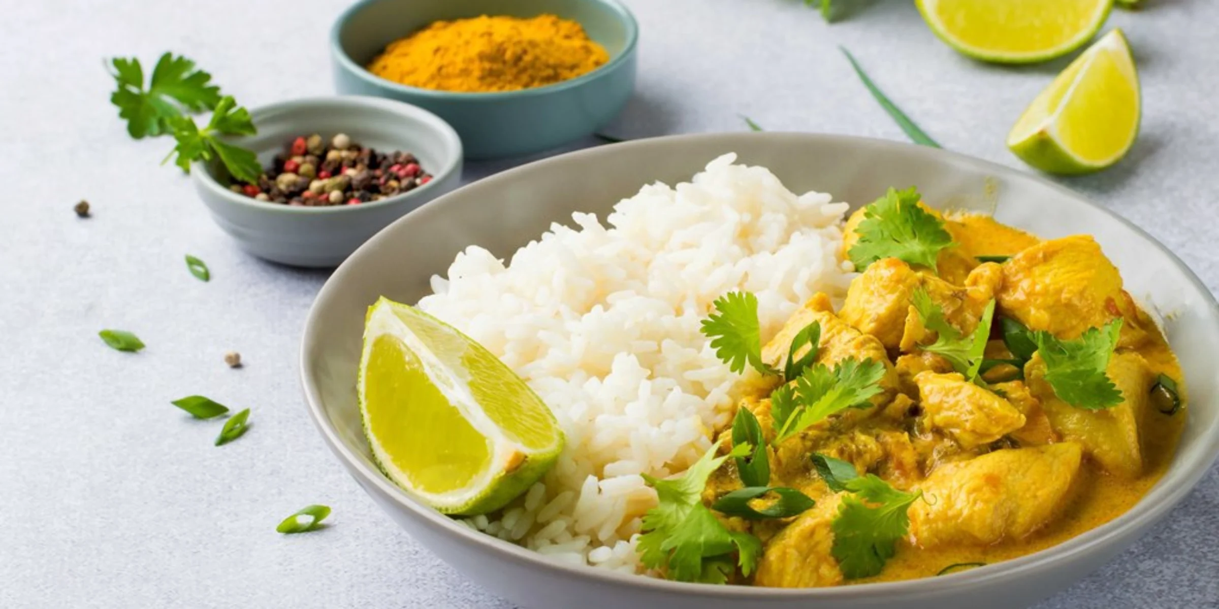 Eine Schüssel mit Curry-Hähnchen, Reis, Limette und Koriander auf einem Tisch.