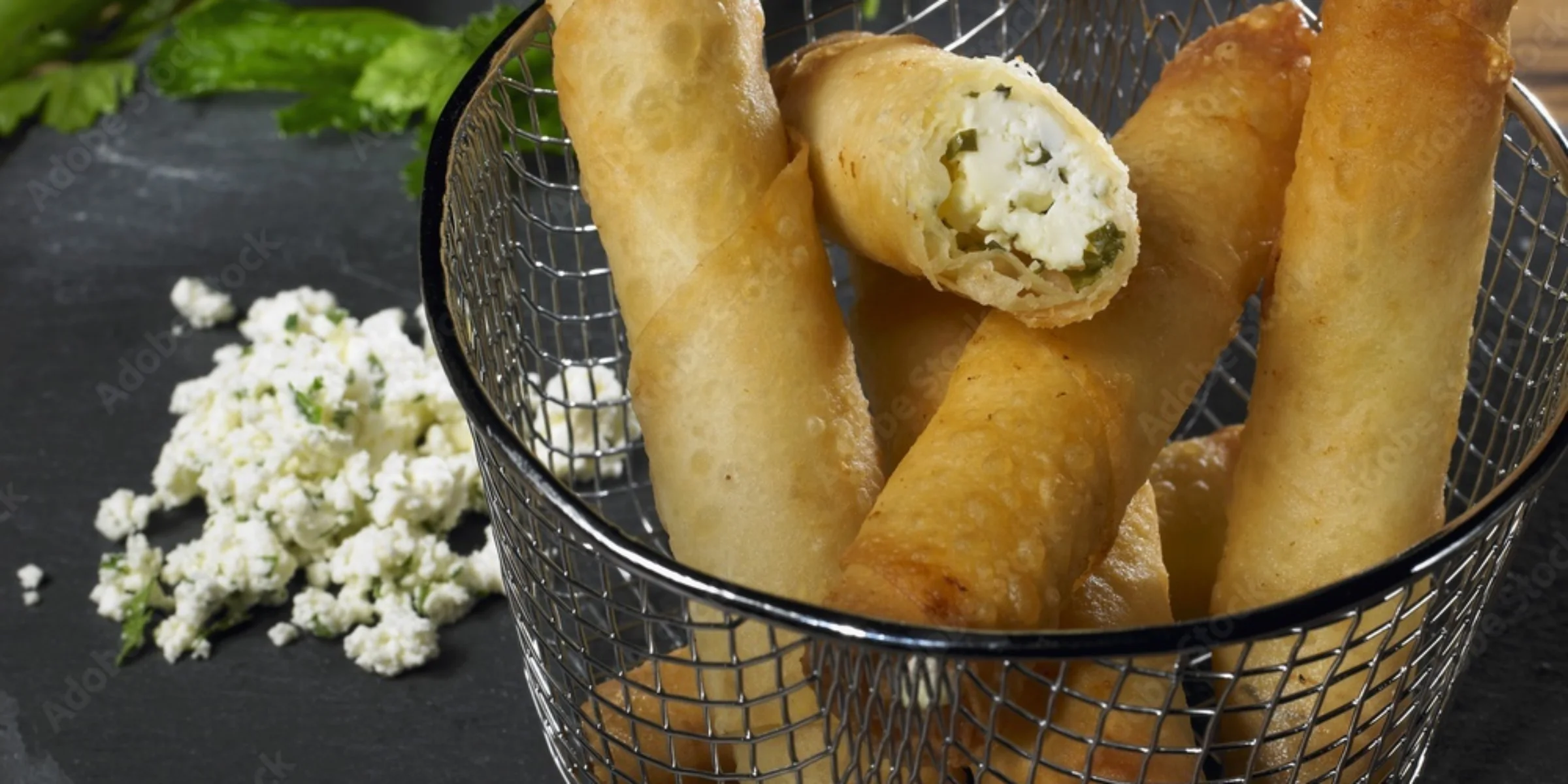 Knusprige Teigröllchen gefüllt mit Käse auf einem Schieferteller, dekoriert mit frischen Kräutern.