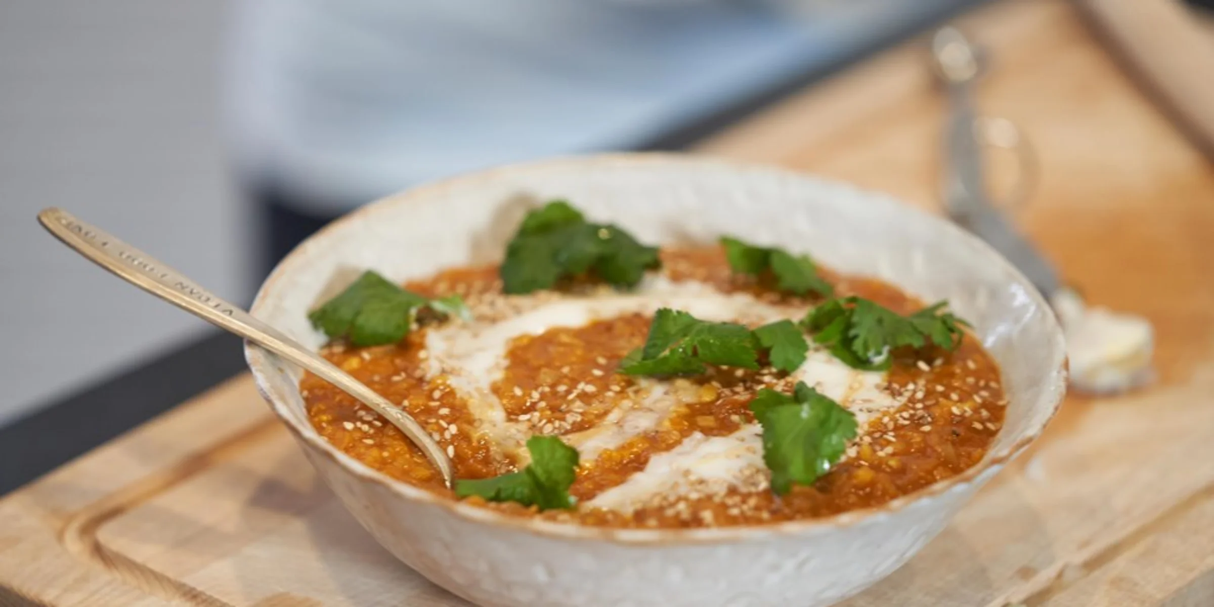 Eine Schüssel mit Linsensuppe, garniert mit Sahne und Koriander, steht auf einem Holzbrett.