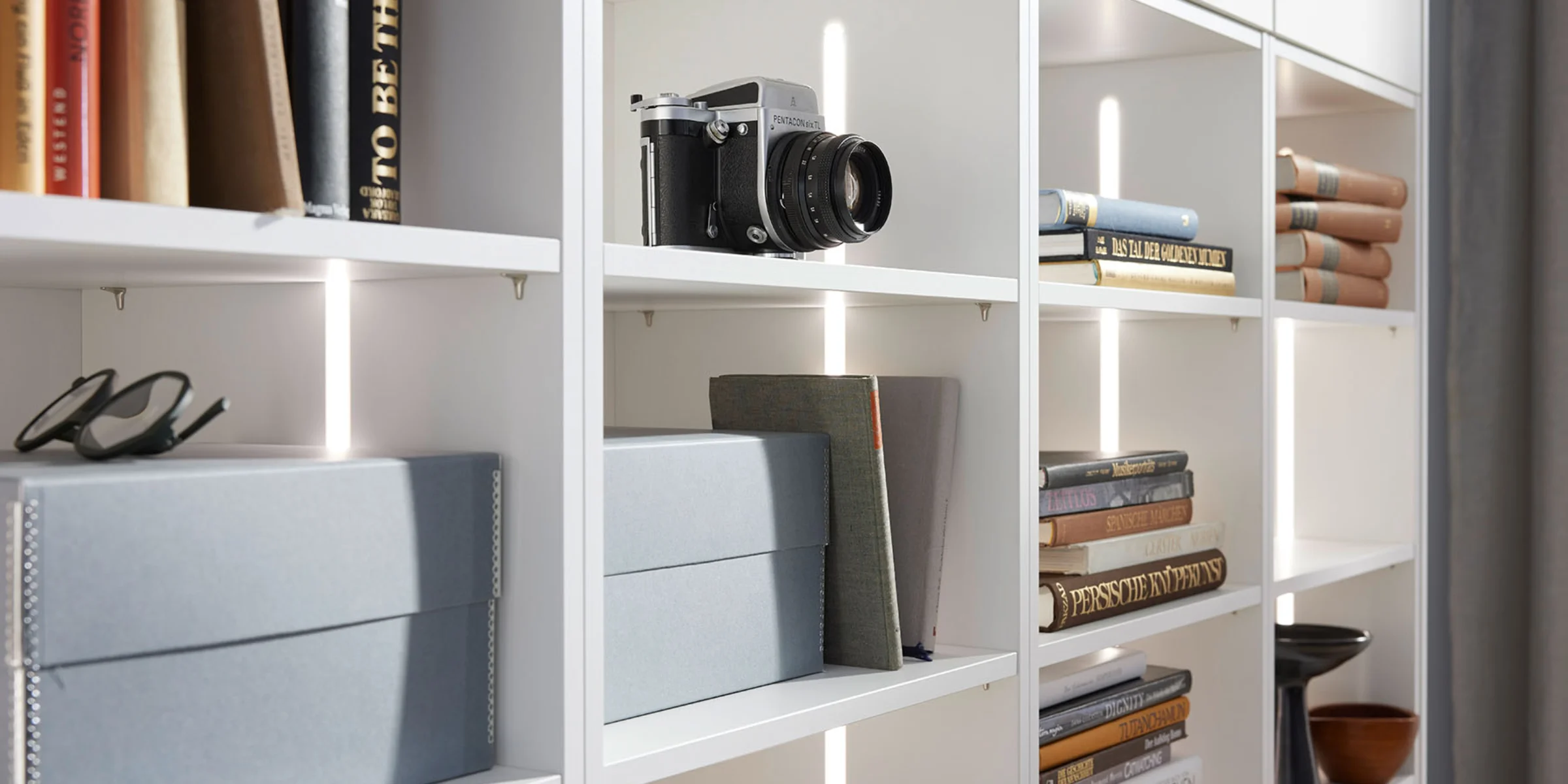 Ein Regal mit Büchern, Kamera und Boxen; ein Beispiel für stilvolle Aufbewahrung von Nolte Living.