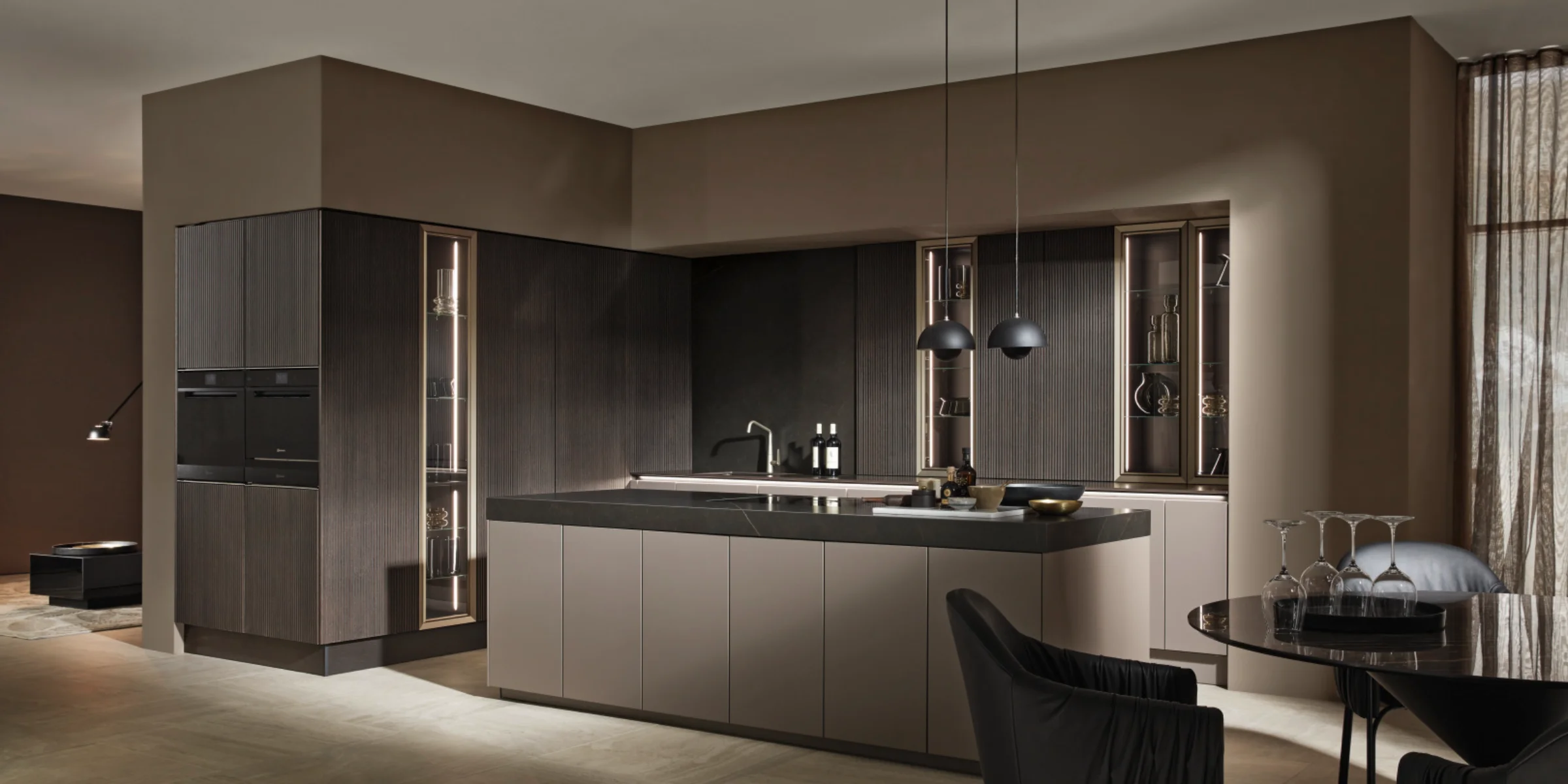 Elegante Nolte Küche mit der exklusiven Front neoLODGE in Eiche geschwärzt gerillt kombiniert mit SOFT LACK in Magma softmatt. Die grifflose Kücheninsel mit dunkler Arbeitsplatte trifft auf hochwertig beleuchtete Vitrinenelemente und sorgt in Verbindung mit den strukturierten Holzelementen für eine edle, wohnliche Atmosphäre im modernen Design.