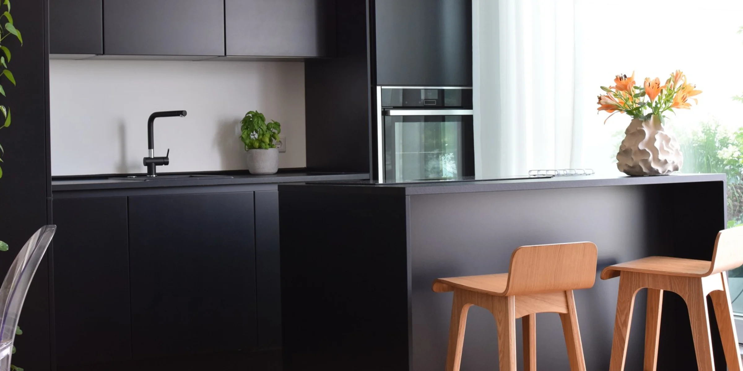 Eine moderne schwarze Küche mit Insel und Holzstühlen, dekoriert mit Pflanzen. Nolte Küchen.