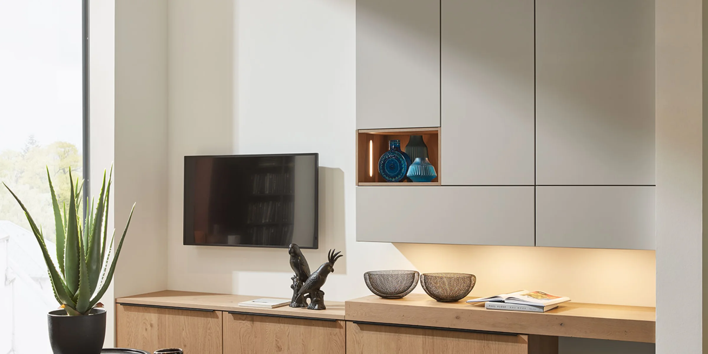 Una sala moderna con elegantes armarios y TV, decorada con plantas y esculturas, Nolte Living.