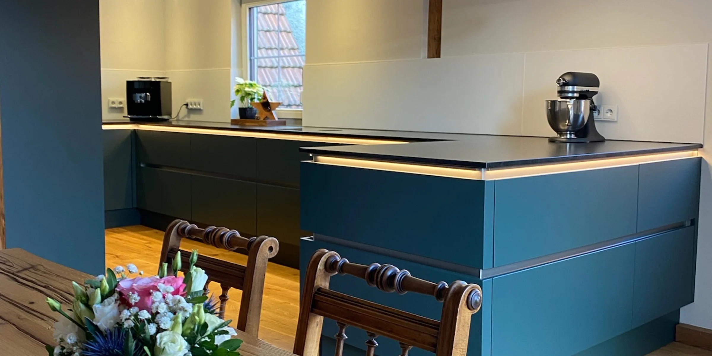 Eine moderne Küche mit Holzbalken und Blumen auf dem Tisch, gestaltet von Nolte Küchen.