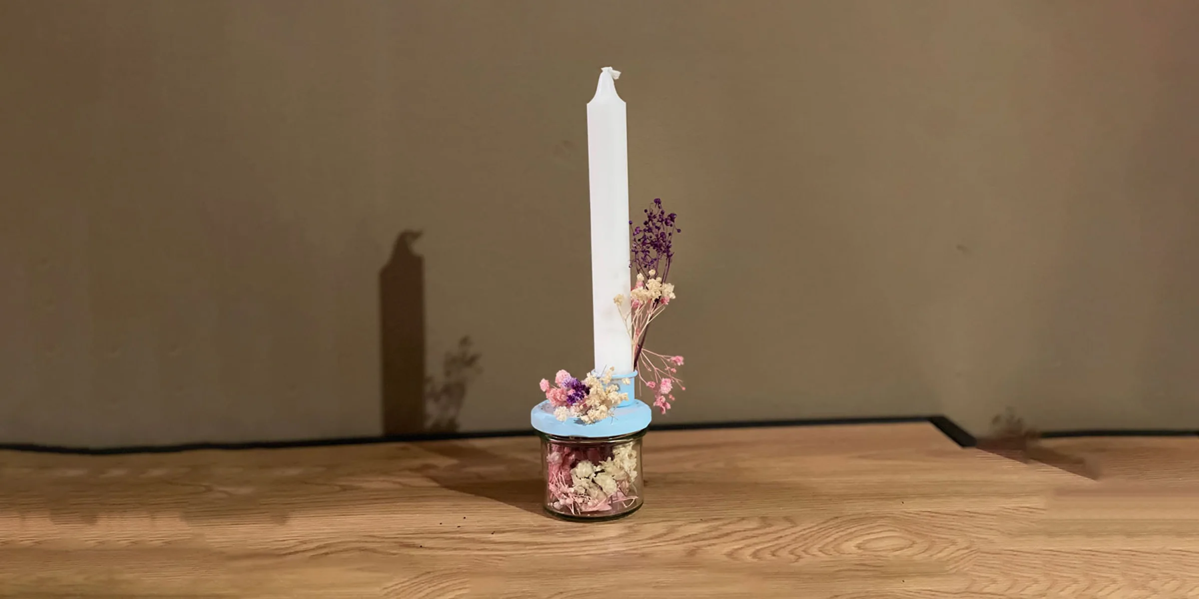 Eine einzelne brennende Kerze steht auf einem Holztisch, dekoriert mit getrockneten Blumen.