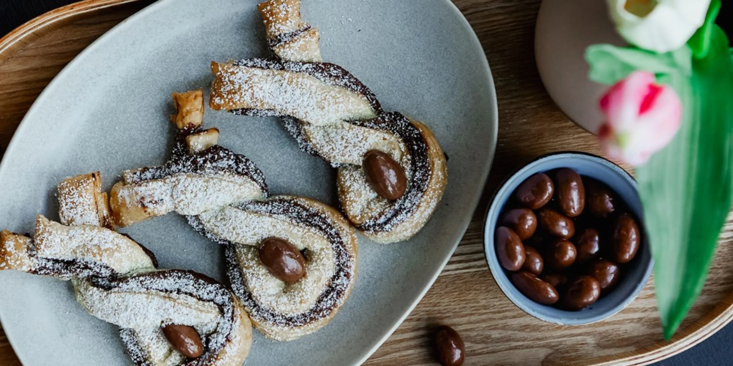 Drei Schokoladen-Gebäckstücke auf einem Teller mit Mandeln, daneben eine Vase mit Blumen.
