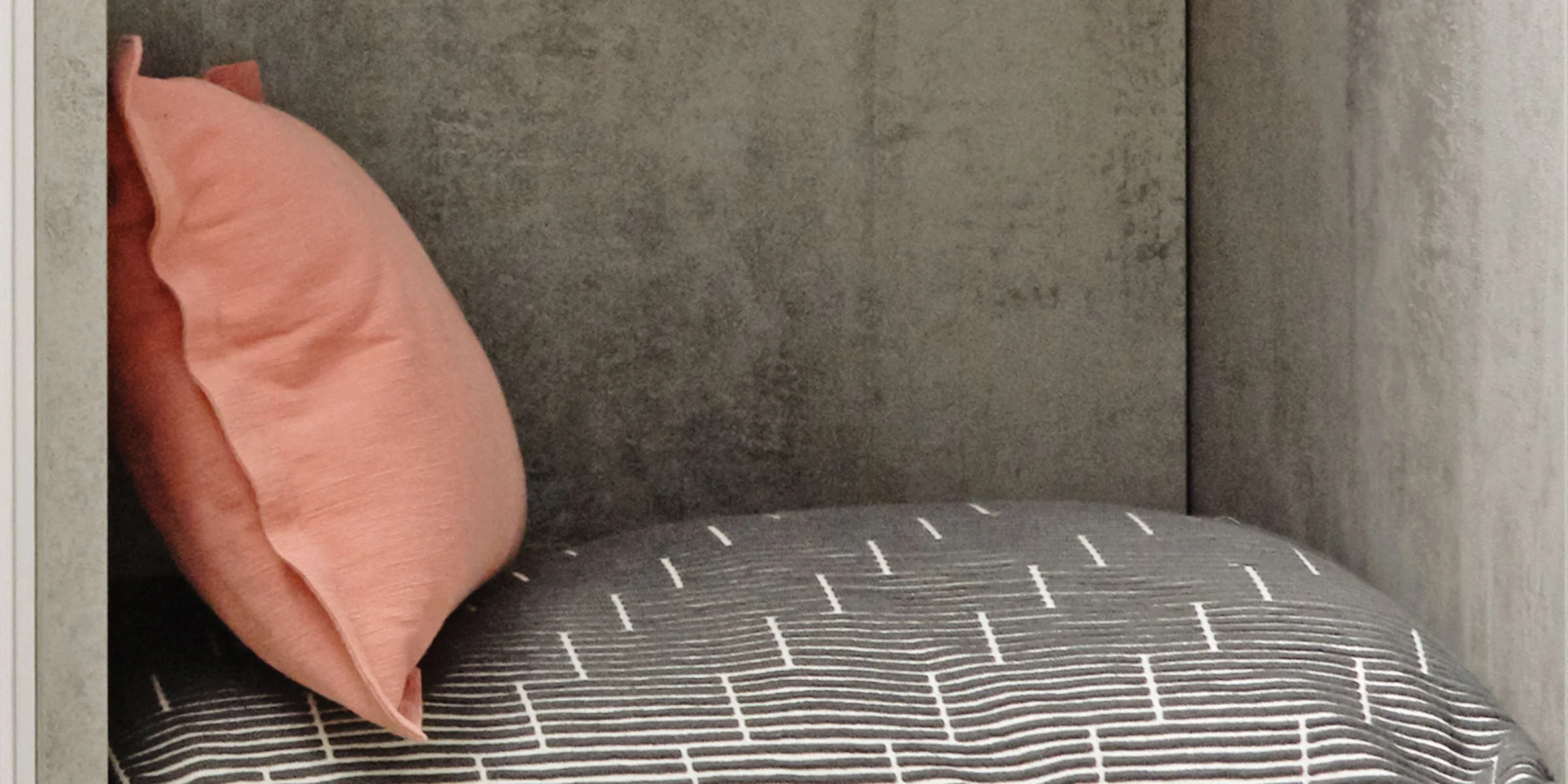 Ein graues Kissen mit weißen Streifen und ein rosa Kissen in einem Regal. Nolte Living.