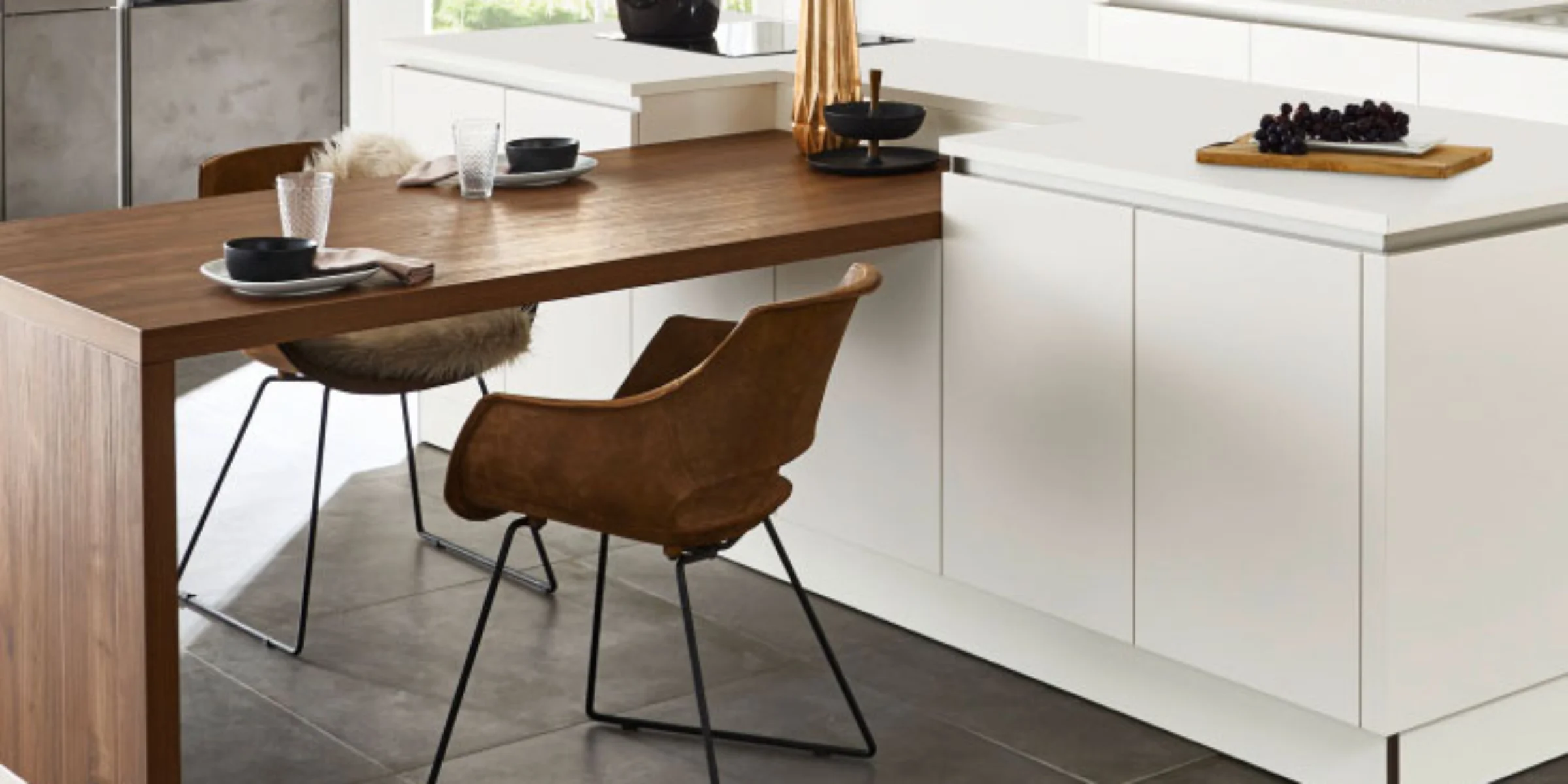 Moderne Küche mit Holz-Esstisch und weißen Schränken, dekoriert mit Geschirr und Blumen. Nolte Küchen.