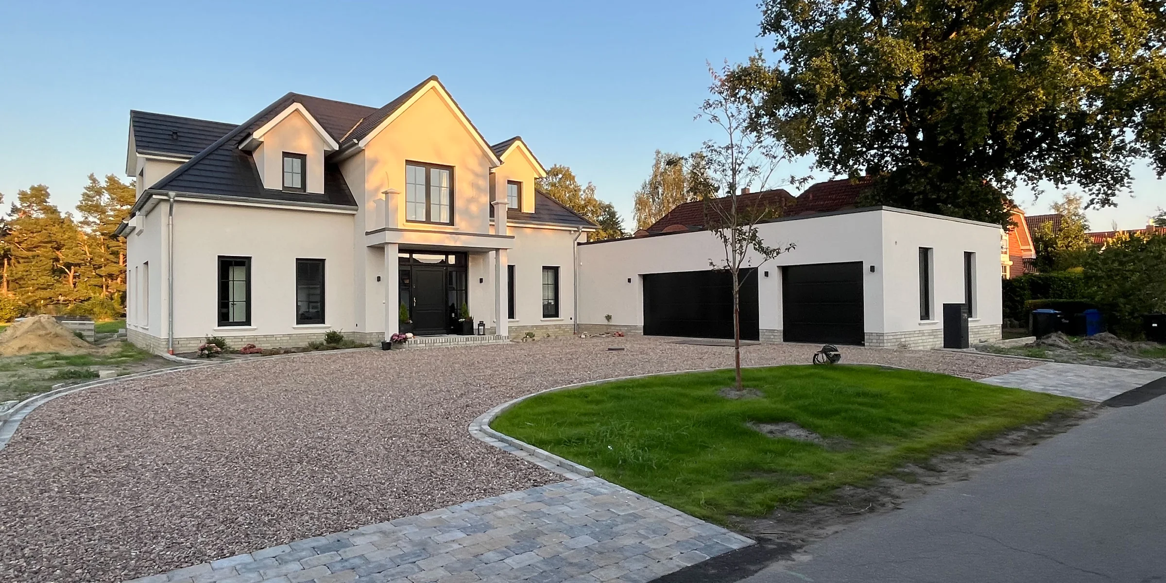 Ein modernes Einfamilienhaus mit großem Vorgarten und gepflasterter Einfahrt bei Sonnenuntergang.
