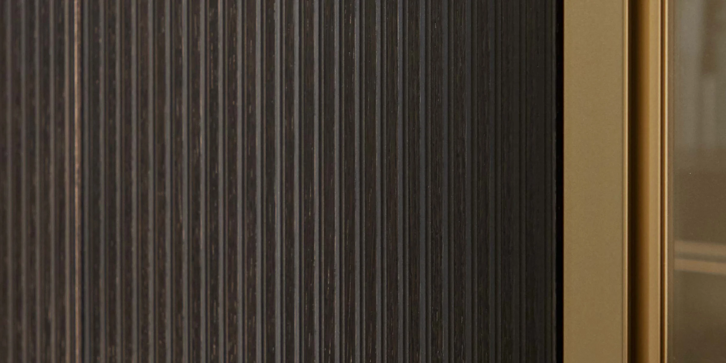 Ein dunkles, geriffeltes Paneel neben einem goldenen Rahmen zeigt exklusives Design von NolteNeo.