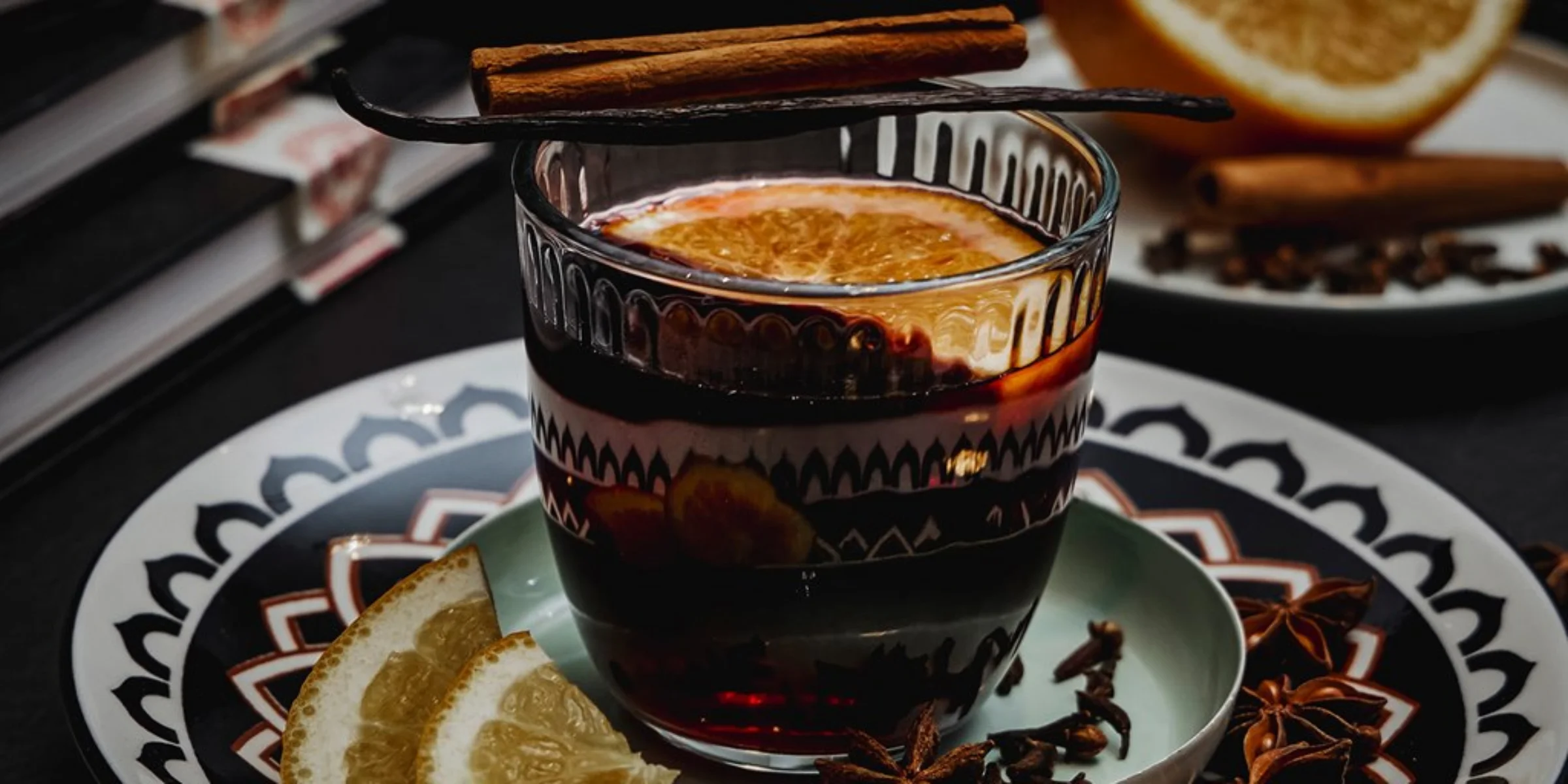 Ein warmes Getränk mit Zitrusscheiben und Zimtstange steht auf einem dekorativen Teller.