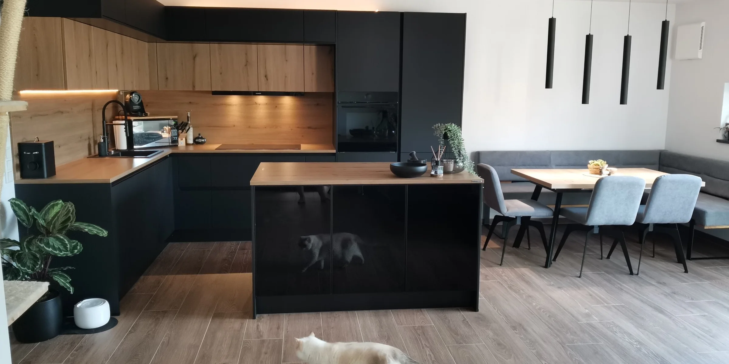 Eine moderne Küche mit Holz- und Schwarzelementen, einer Insel und einem Tisch; Nolte Küchen.