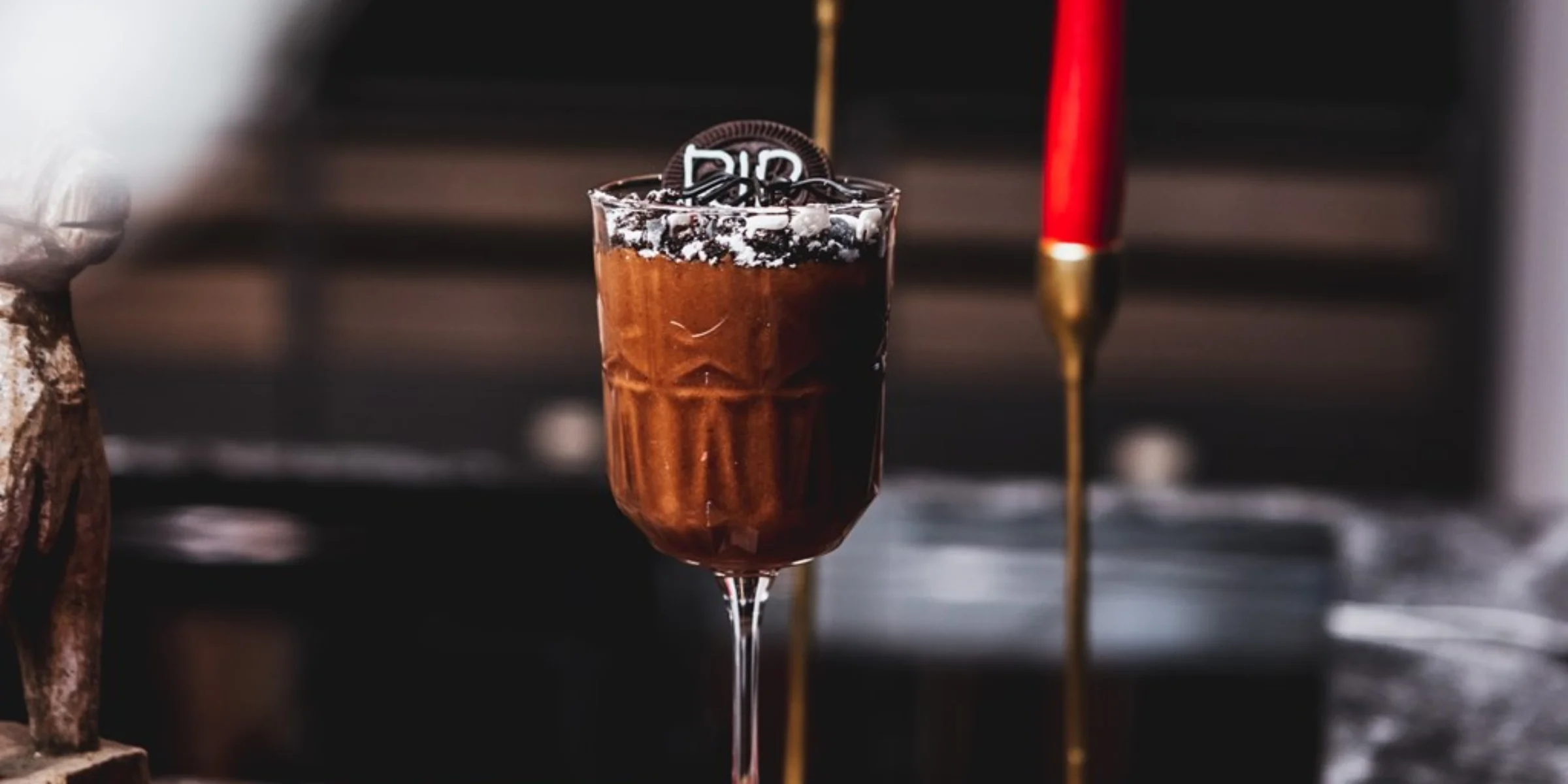 Ein Glas Schokoladenmousse mit Keksen steht auf einem Tisch, im Hintergrund sind rote Kerzen zu sehen.