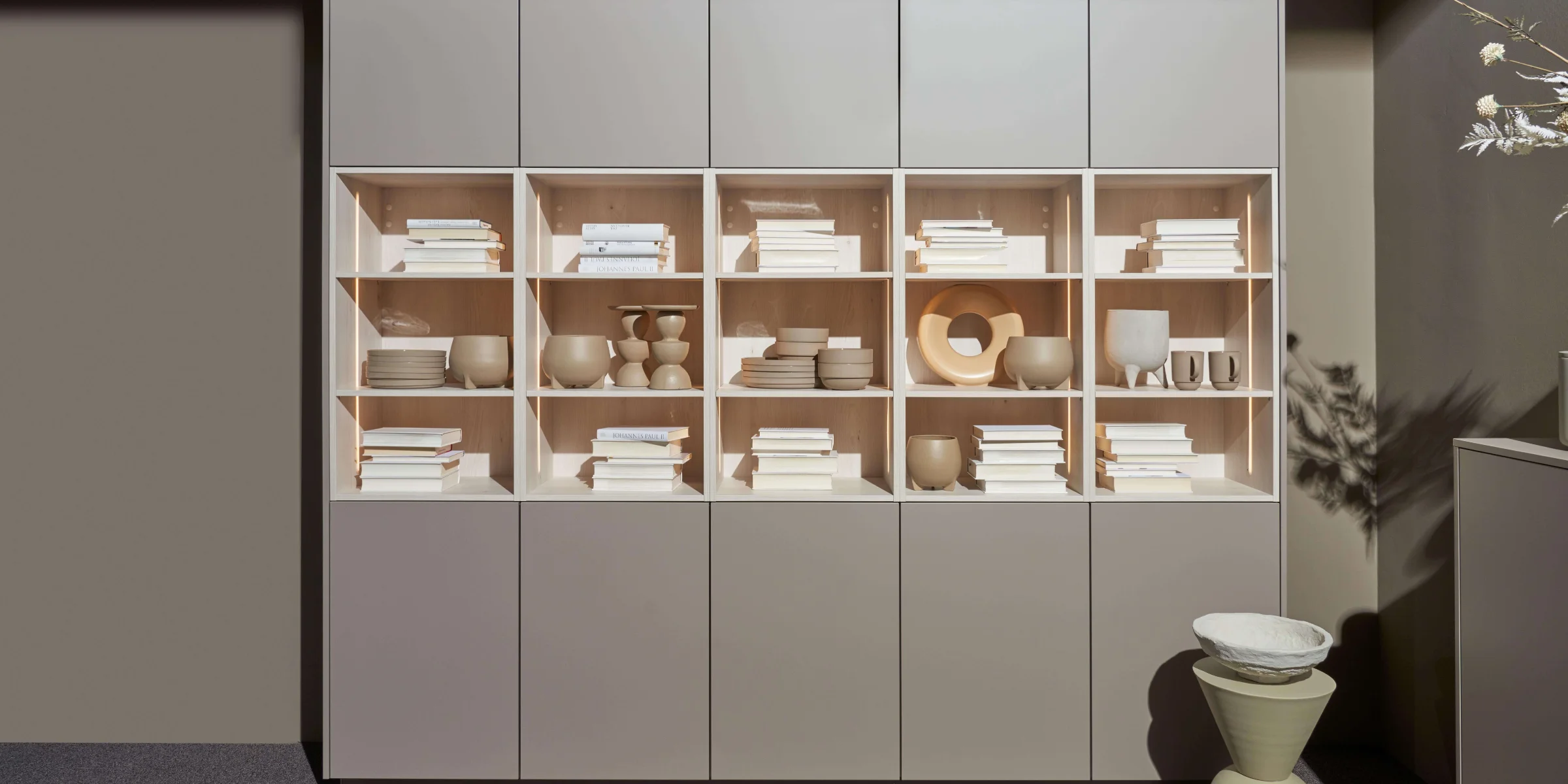 Ein Regal mit dekorativen Vasen und Büchern in einem modernen Design, präsentiert von Nolte Living.