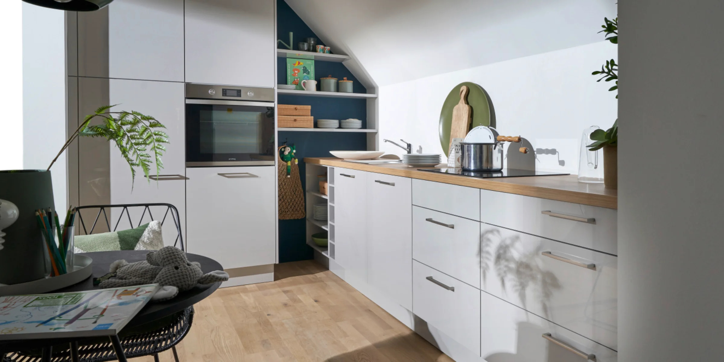 Cuisine moderne avec armoires blanches et plan de travail en bois sous pente de toit. Nolte Kitchen.